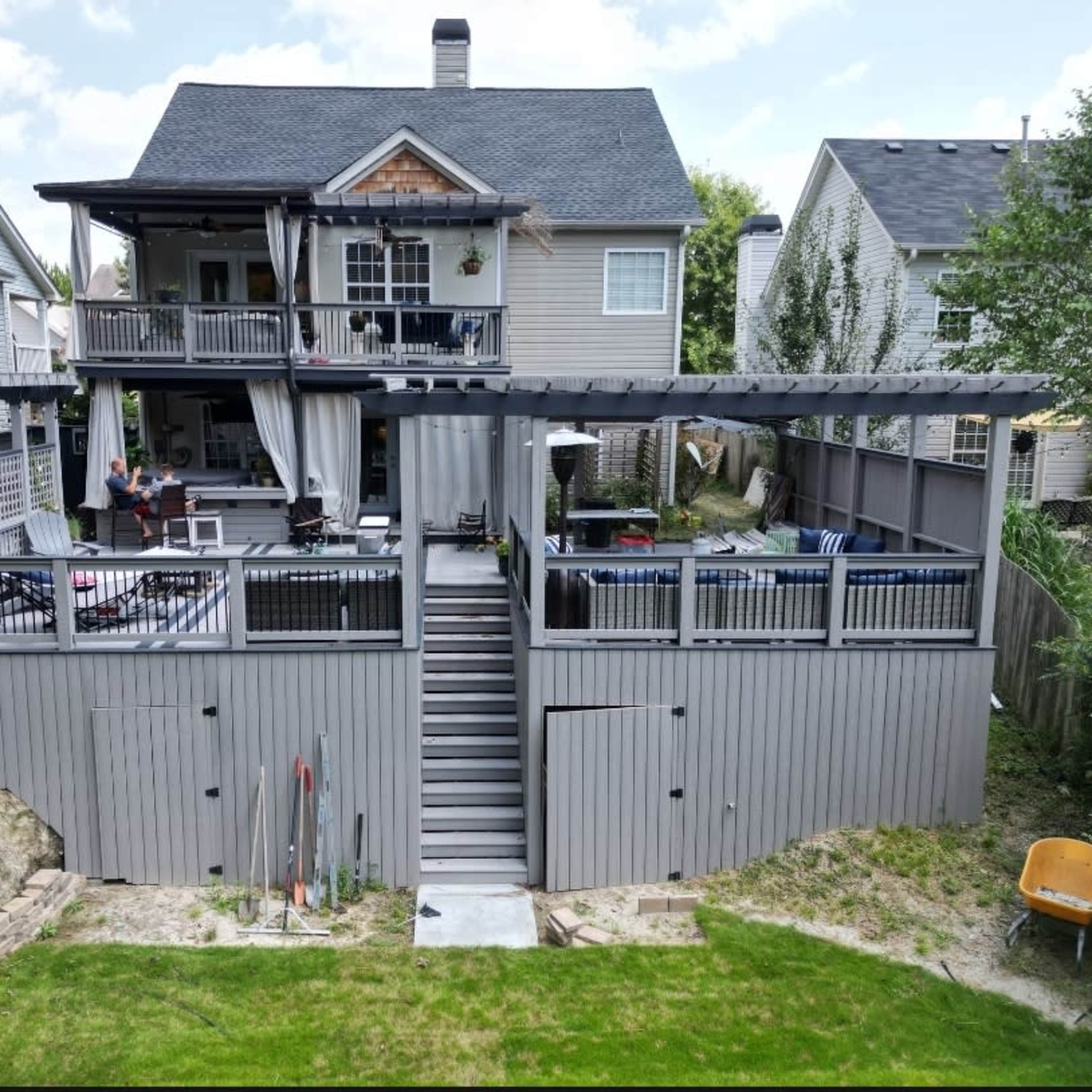 A two-story house with a large backyard deck, featuring multiple seating areas and staircases leading to the ground level.