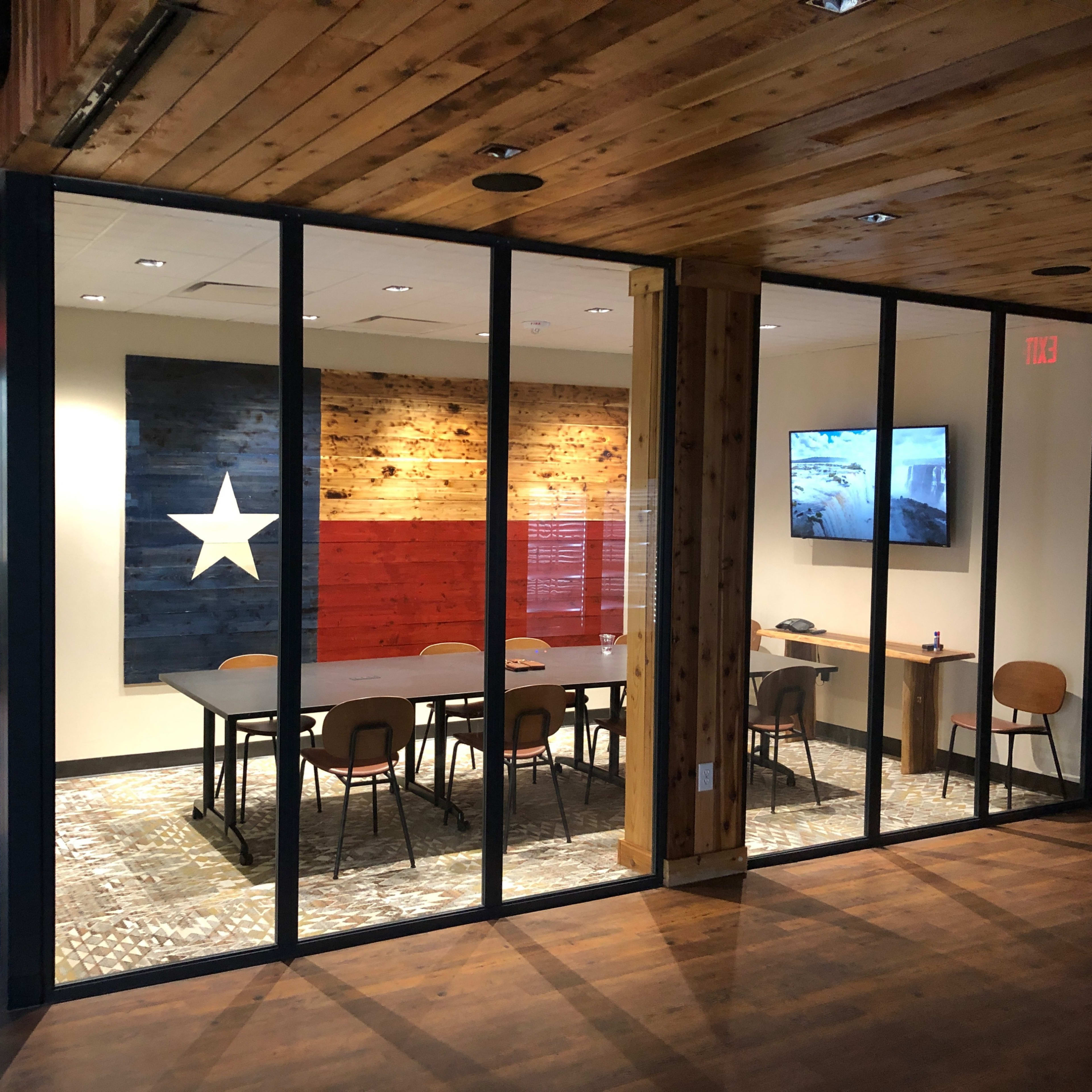 A conference room with glass walls featuring a large wooden wall art of the Texas flag and a television mounted on the side.
