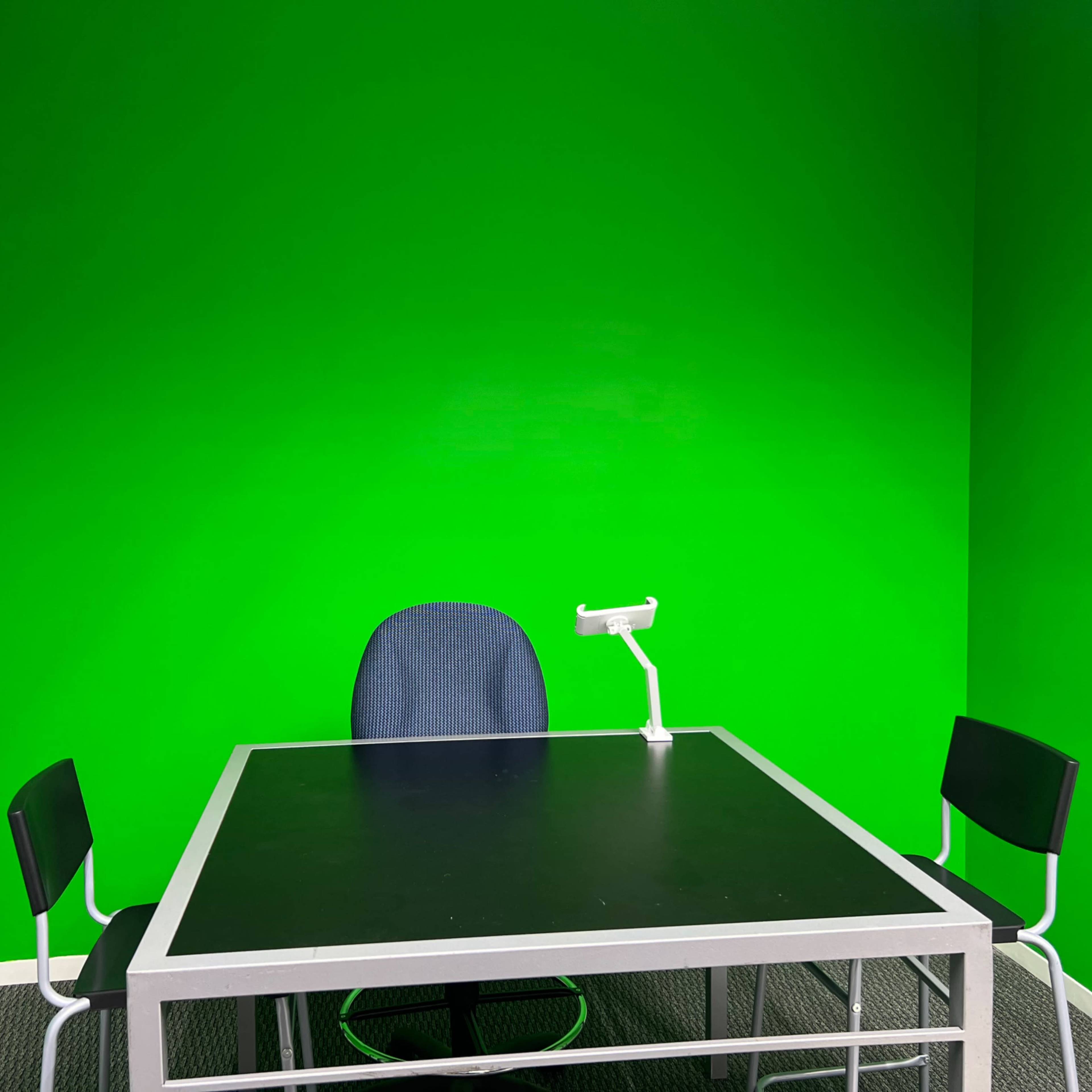 A room with a bright green wall, a black table, a blue office chair, and two black chairs.