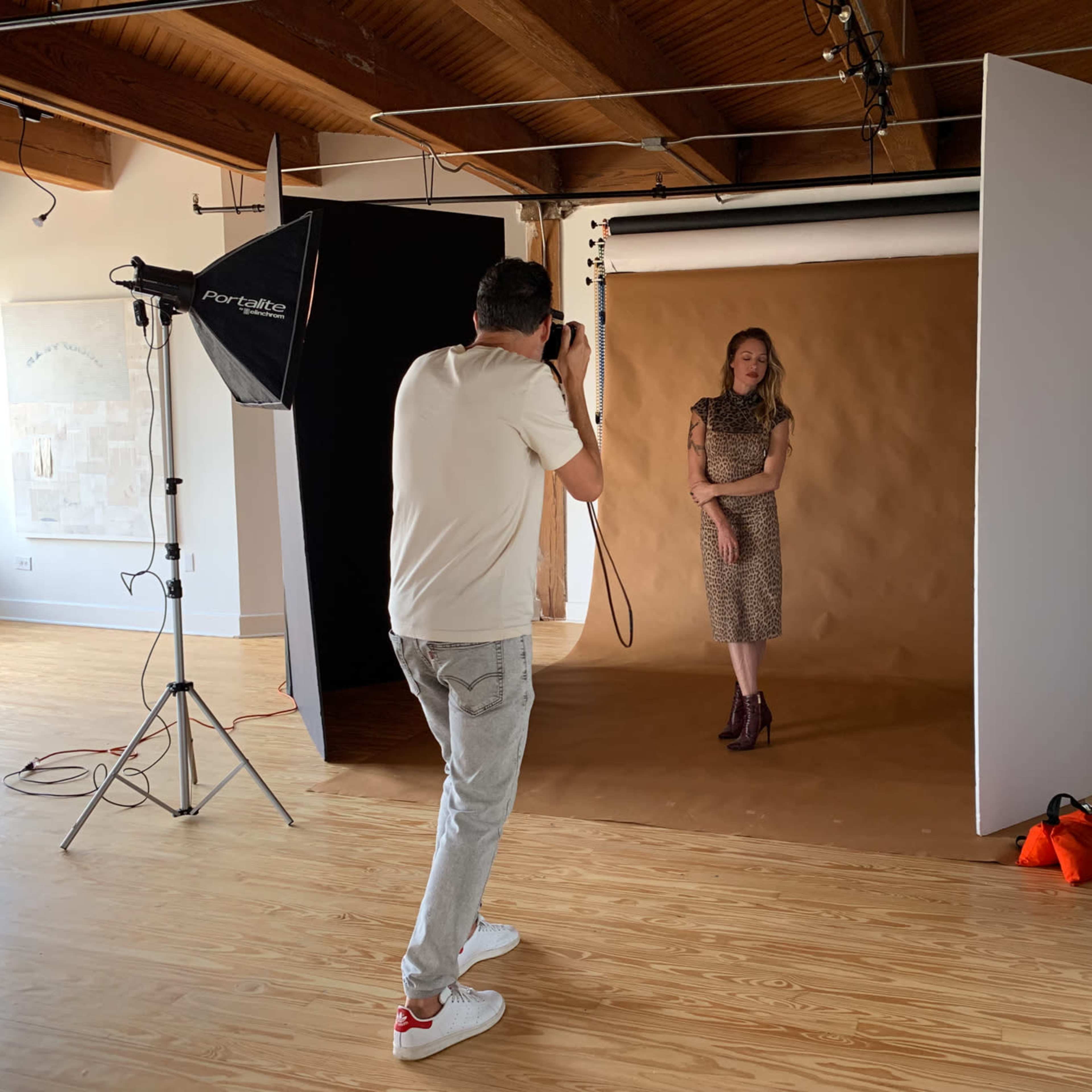 A photographer captures a model posing in front of a brown backdrop in a well-lit studio.