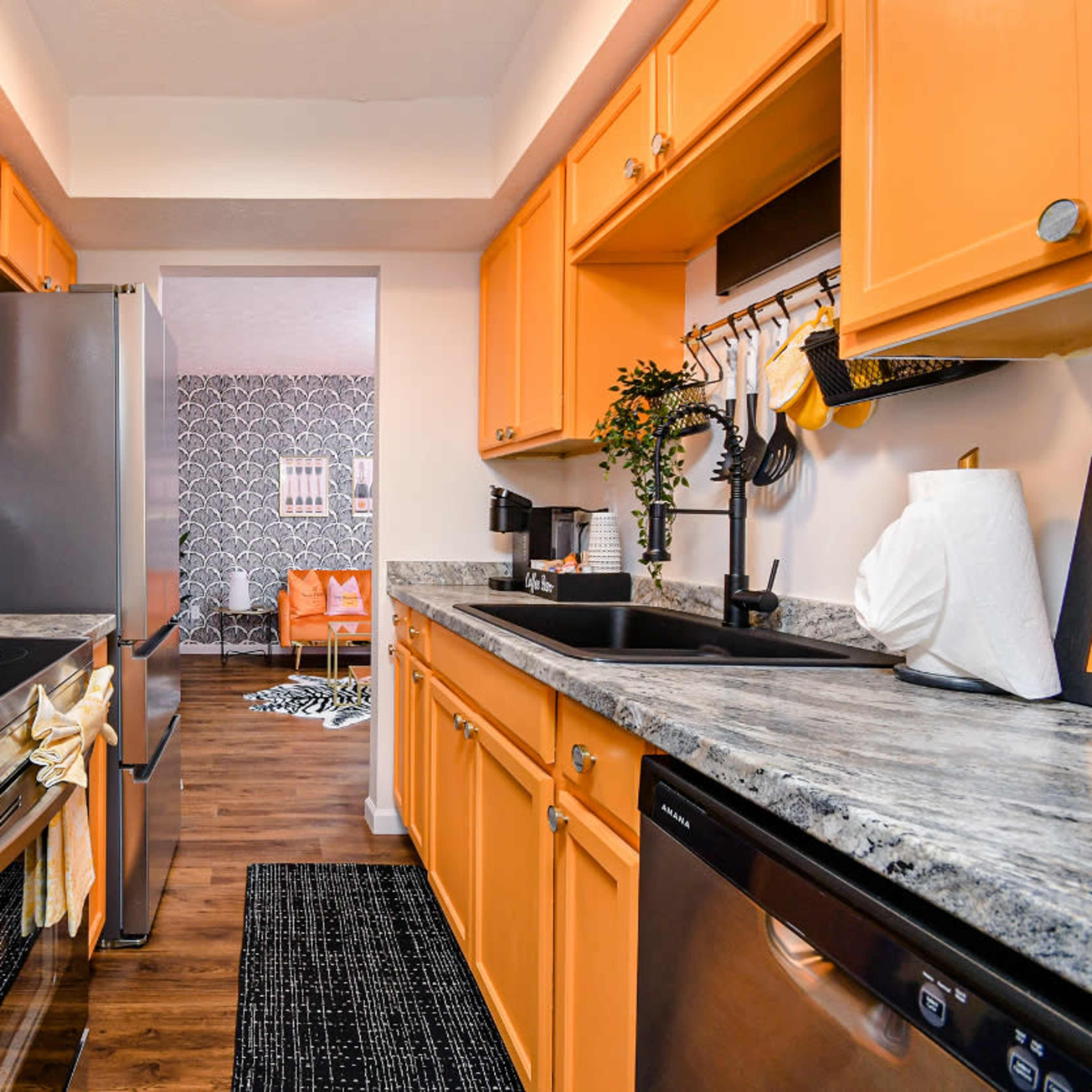 The kitchen features orange cabinets, stainless steel appliances, and a view into a room with patterned wallpaper.