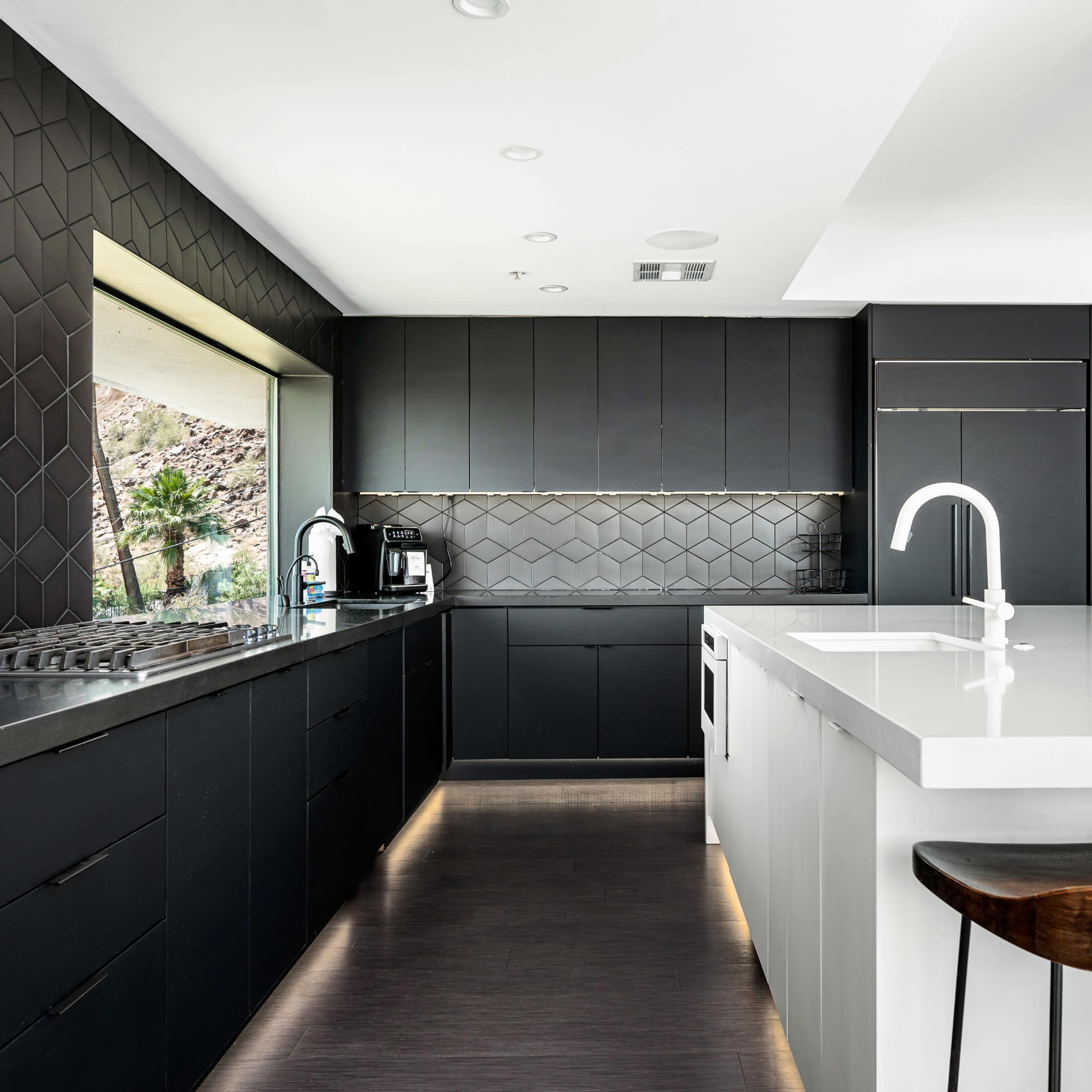 The kitchen features black cabinetry, a large white island, and modern appliances, with a window providing natural light.