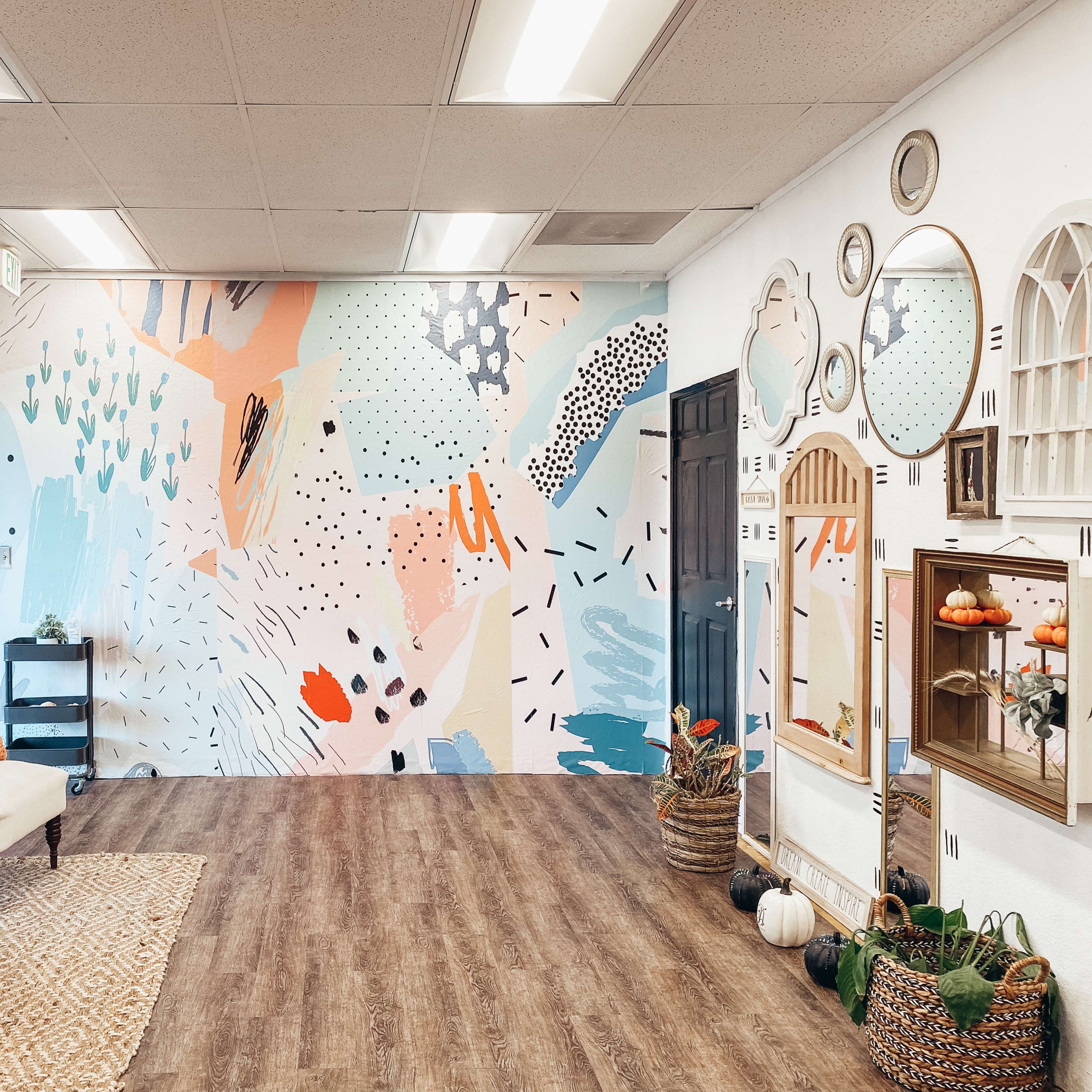 A brightly decorated room featuring a colorful abstract mural, a mirrored cabinet, a sofa with pillows, and various decorative elements, including pumpkins and a woven rug.