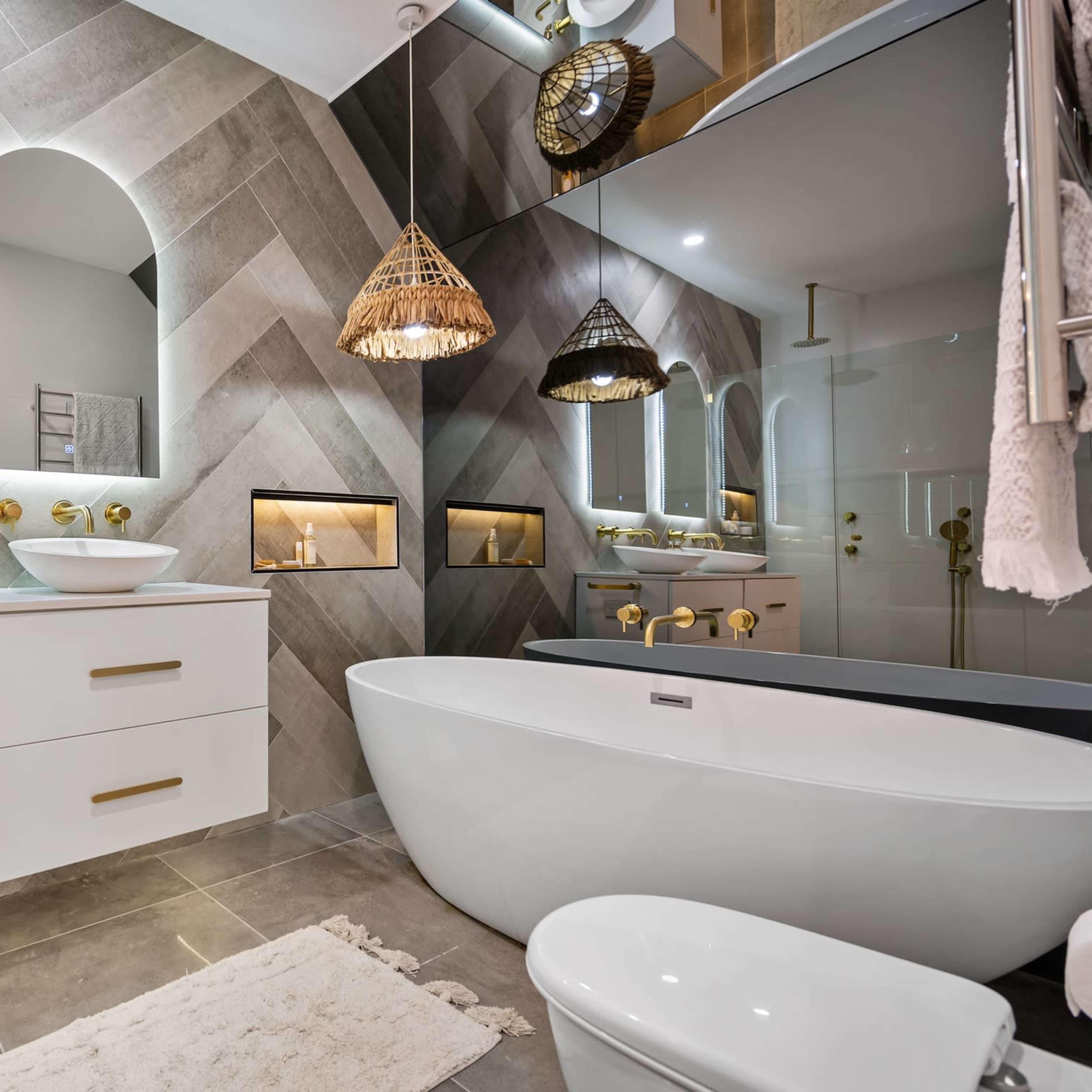 The bathroom features dual mirrors above a white vanity with gold fixtures, a freestanding tub, and textured tiled walls with built-in niches.
