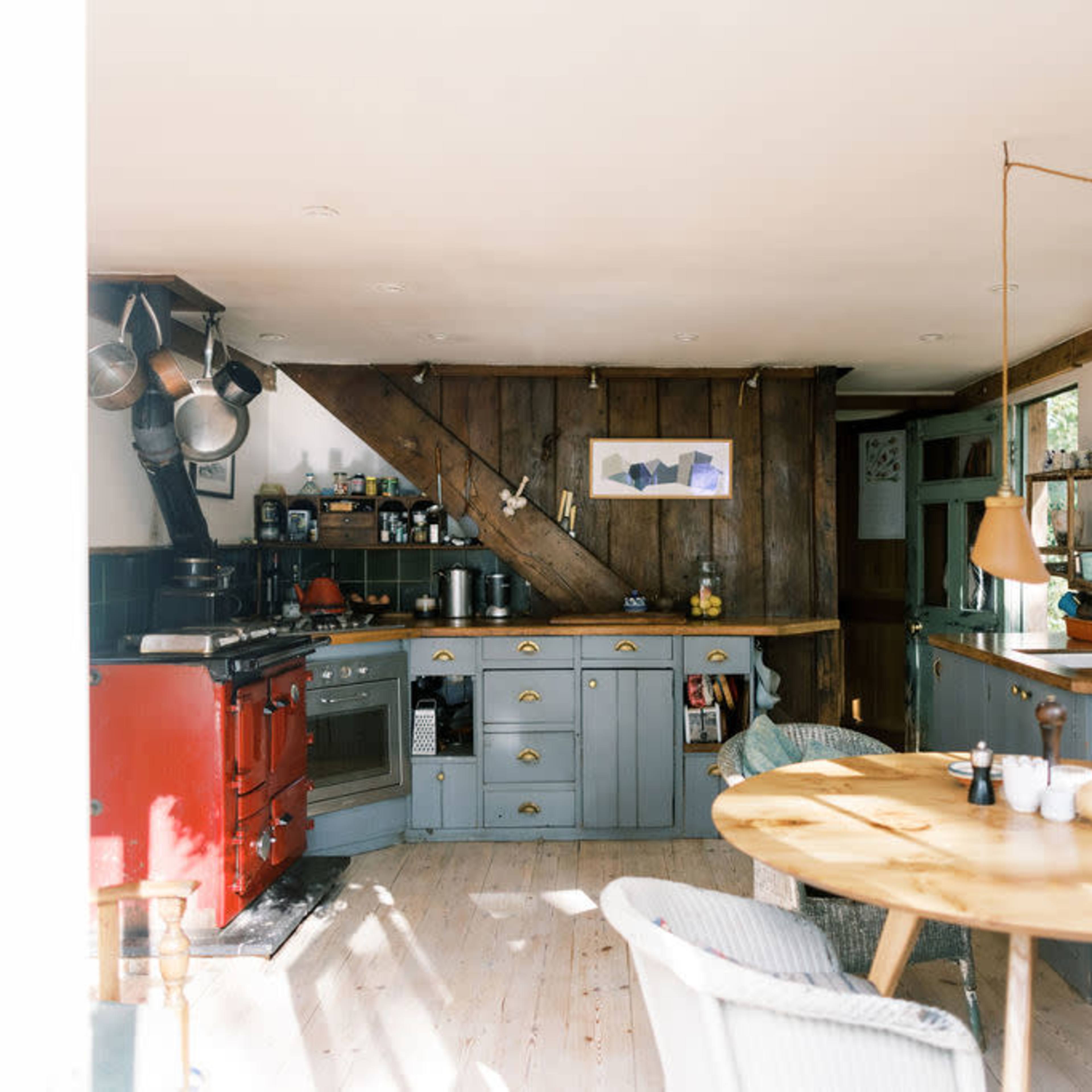 A cozy kitchen features a red stove, gray cabinetry, wooden accents, and a round dining table.