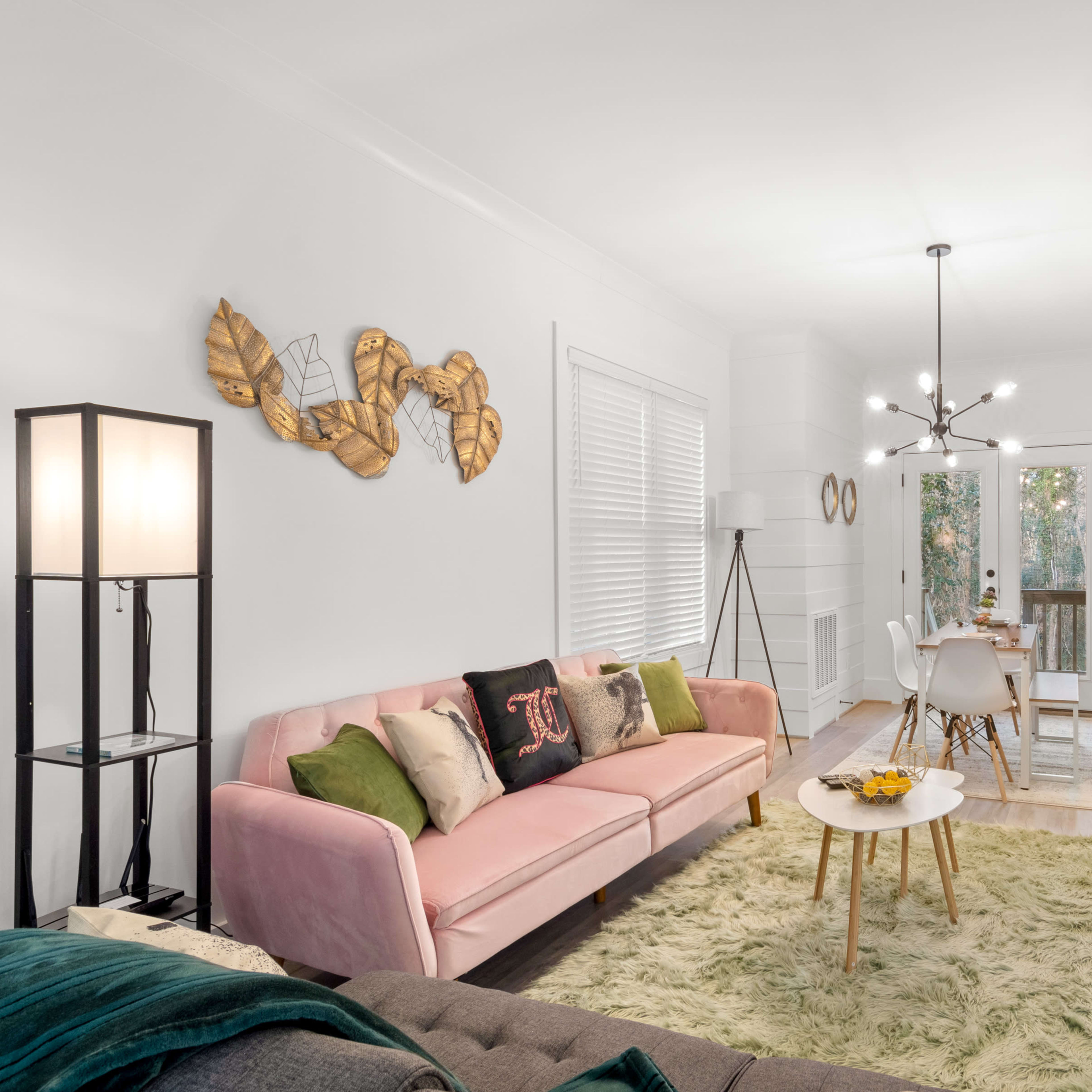 A bright living room featuring a pink sofa, a wooden coffee table with fruit, and a dining area visible in the background.