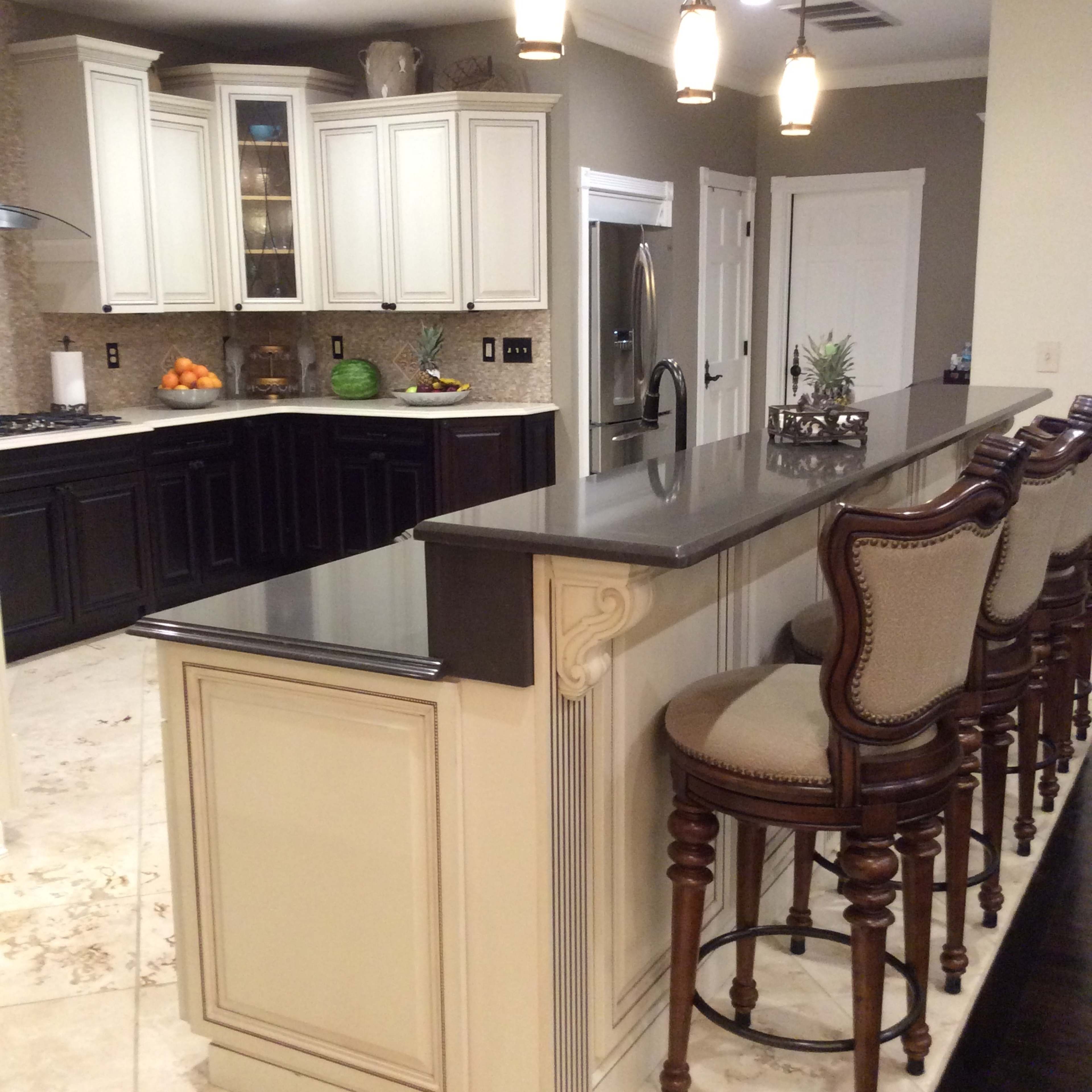 A kitchen featuring a large island with a dark countertop and several barstools, surrounded by cabinetry and appliances.