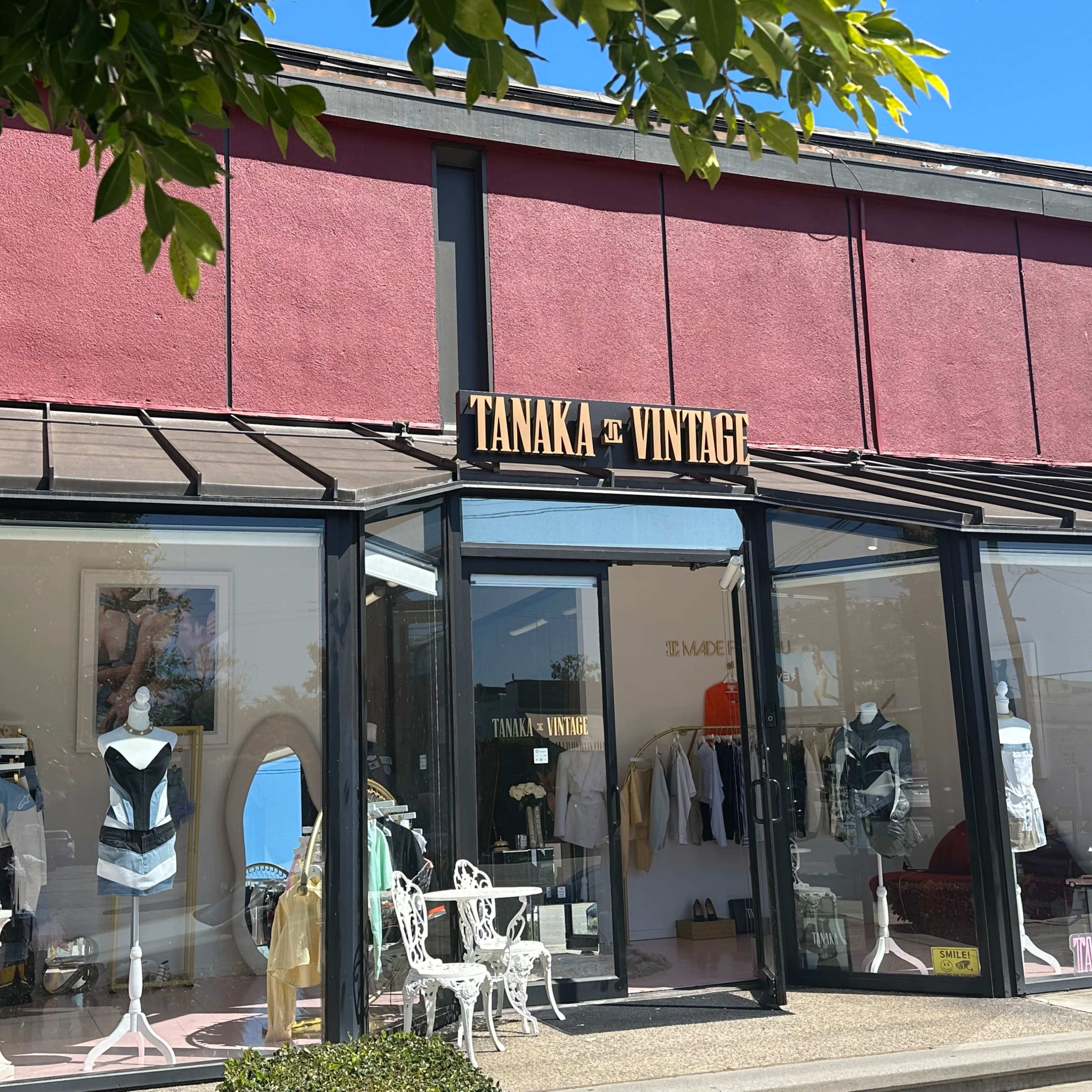 The storefront of Tanaka Vintage features large glass windows displaying vintage clothing and accessories, with outdoor seating in front.
