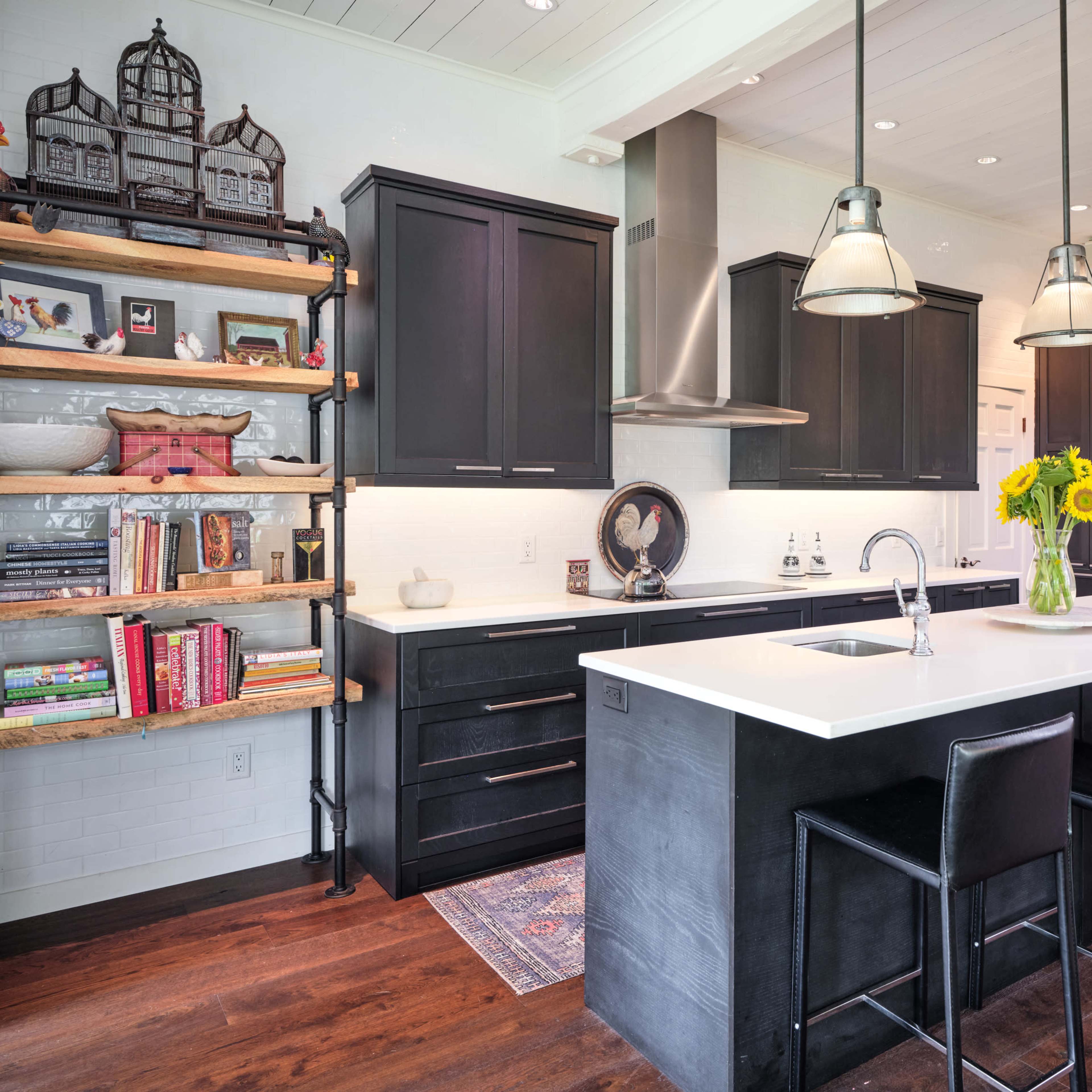 A modern kitchen features black cabinetry, a large white island with seating, and a vase of sunflowers on the counter, complemented by open shelving and stainless steel appliances.