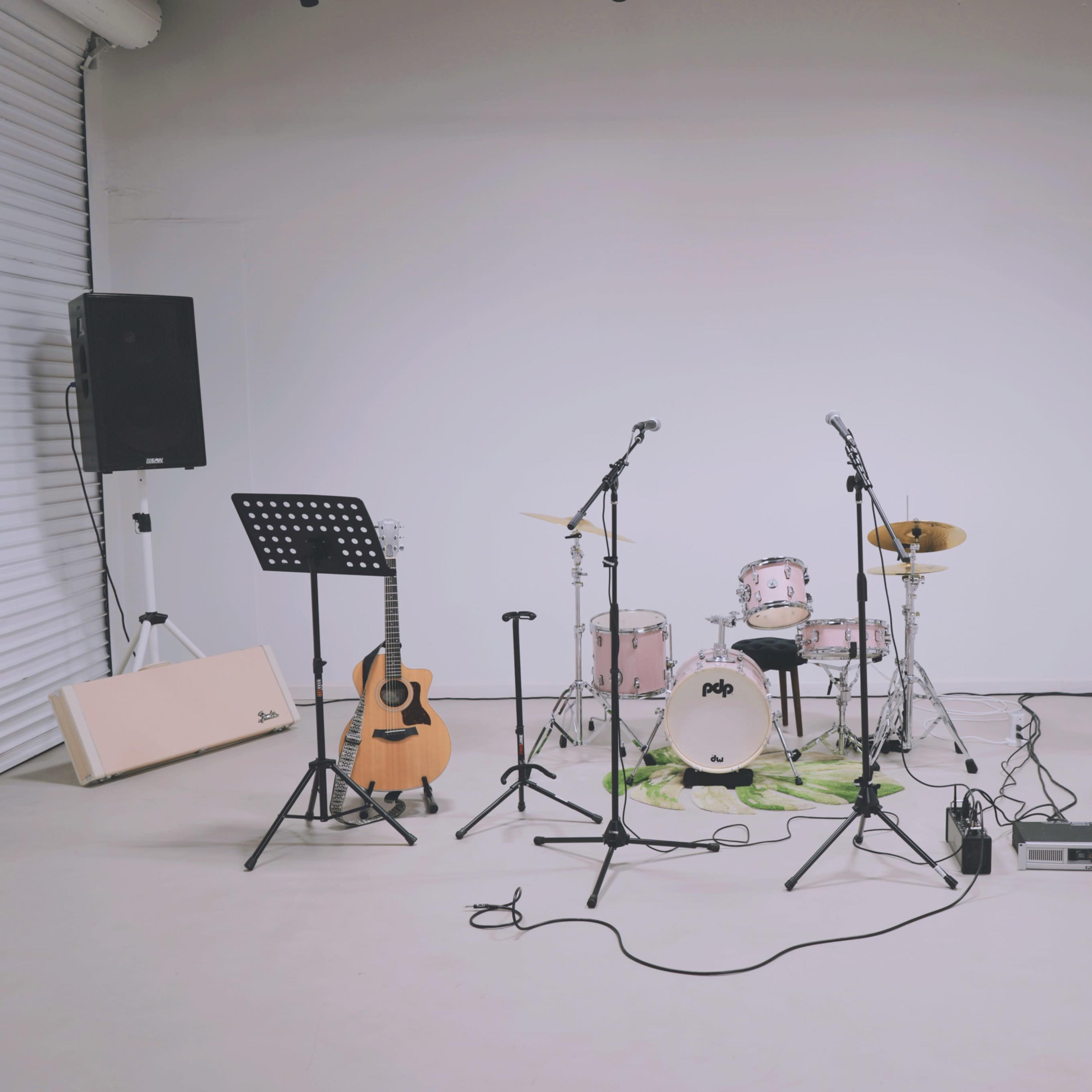 A music setup is arranged in a studio, featuring a drum kit, electric and acoustic guitars, microphones, and speakers.