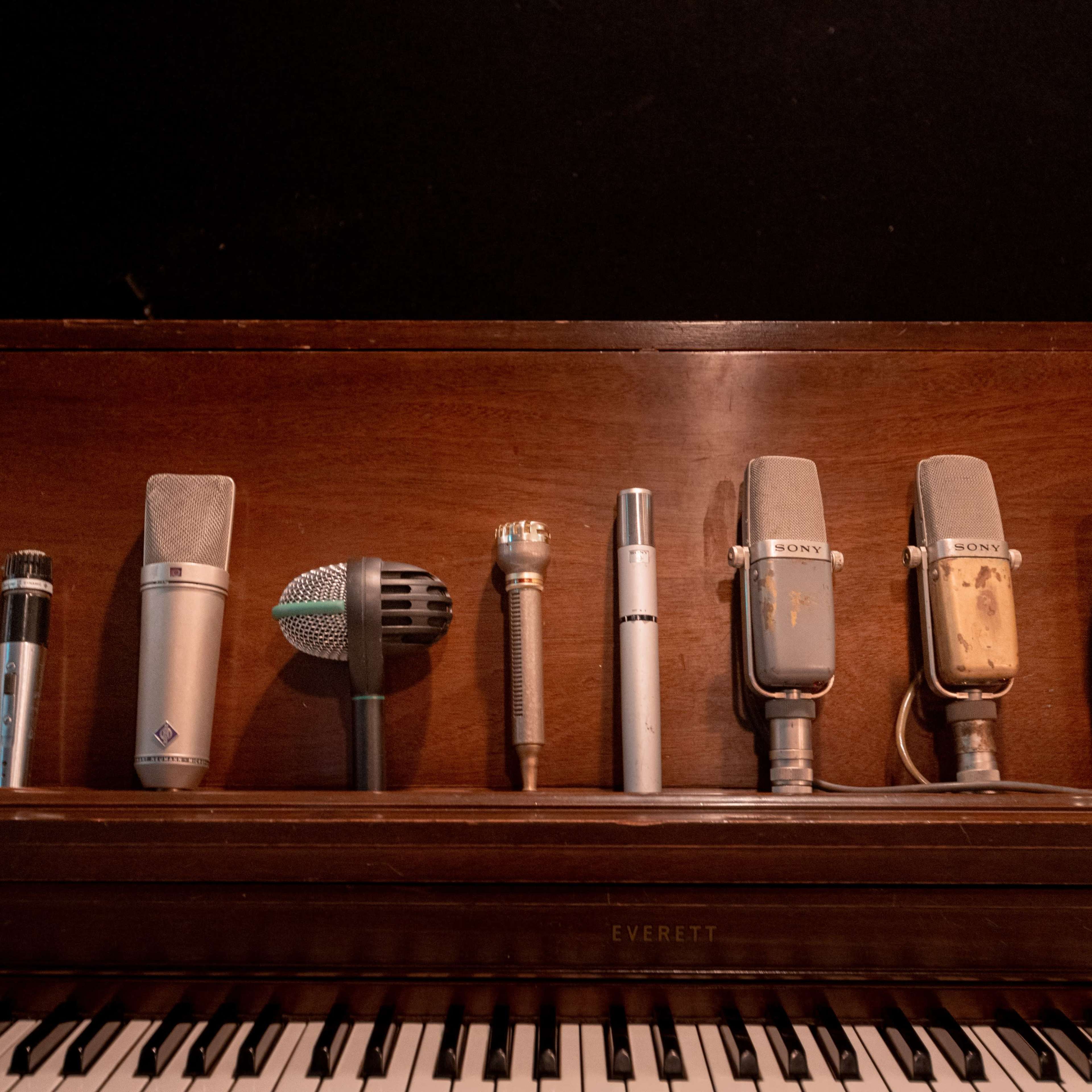 A row of various microphones is placed on a wooden piano.