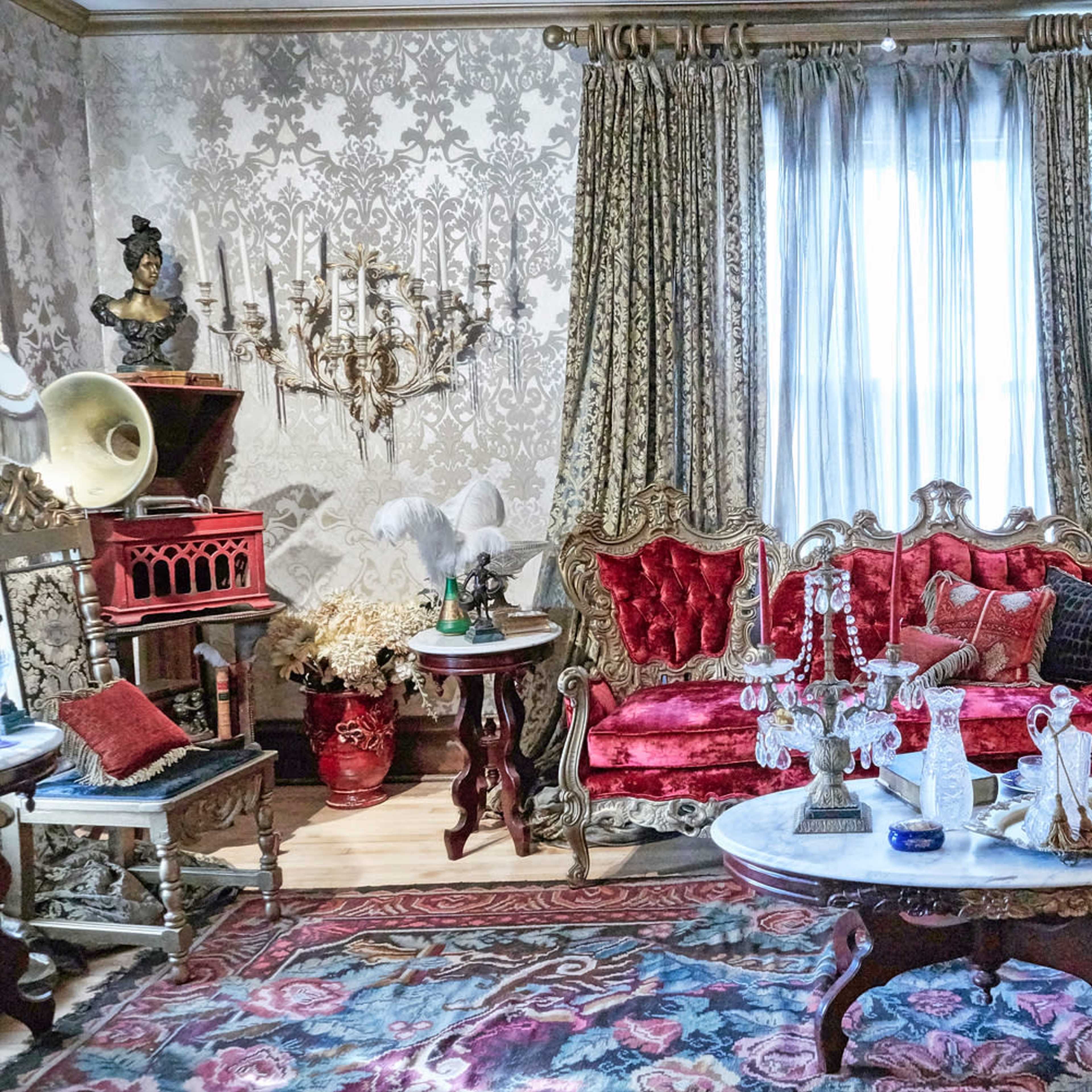 The living room features a red velvet sofa, an ornate chandelier, and a marble coffee table amidst floral-patterned wallpaper.