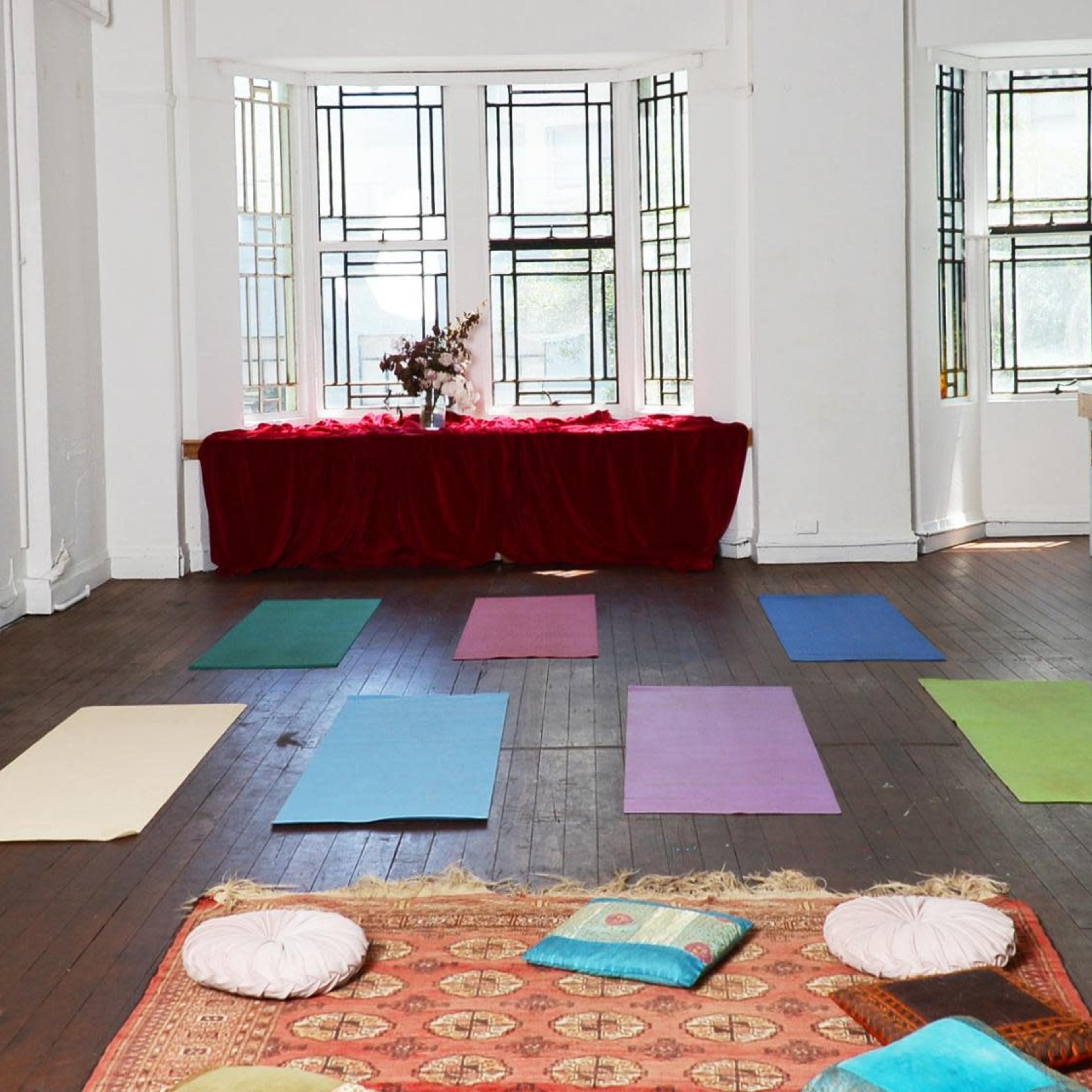 A spacious yoga studio features several exercise mats arranged on a wooden floor with large windows letting in natural light.
