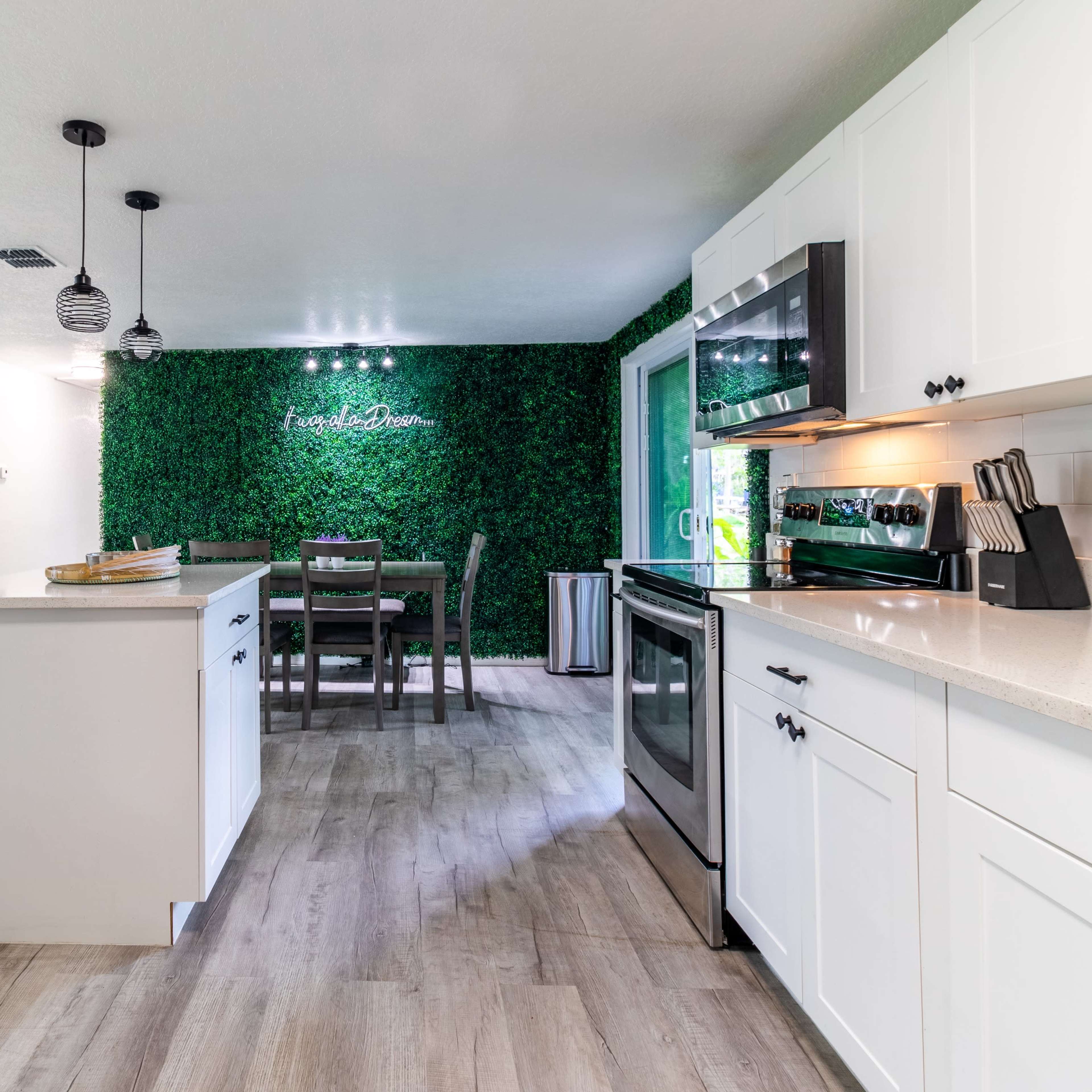 A modern kitchen and dining area with white cabinetry, a countertop, and a green wall feature.