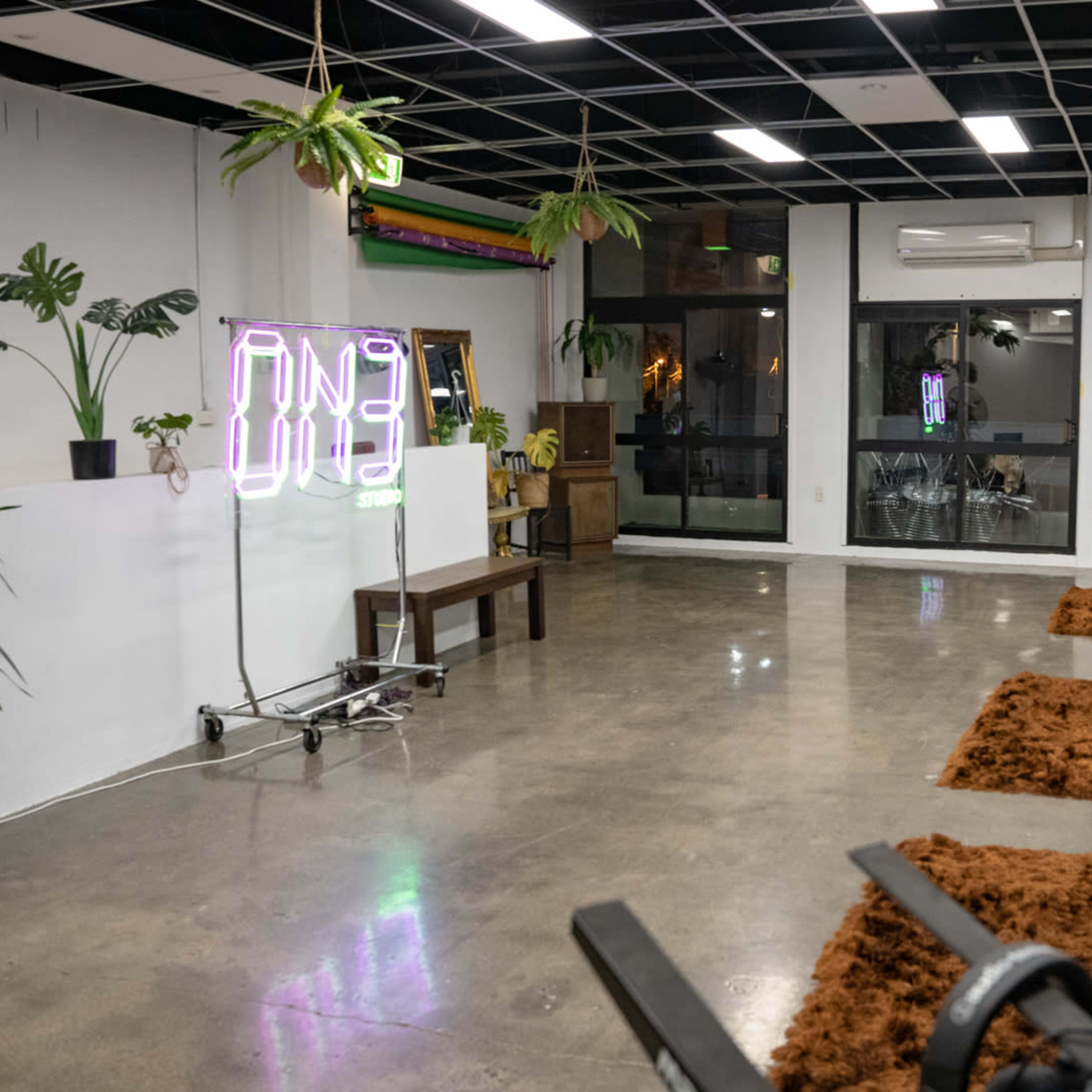 An empty room with a polished concrete floor, two tables, plants in pots, and a neon sign.