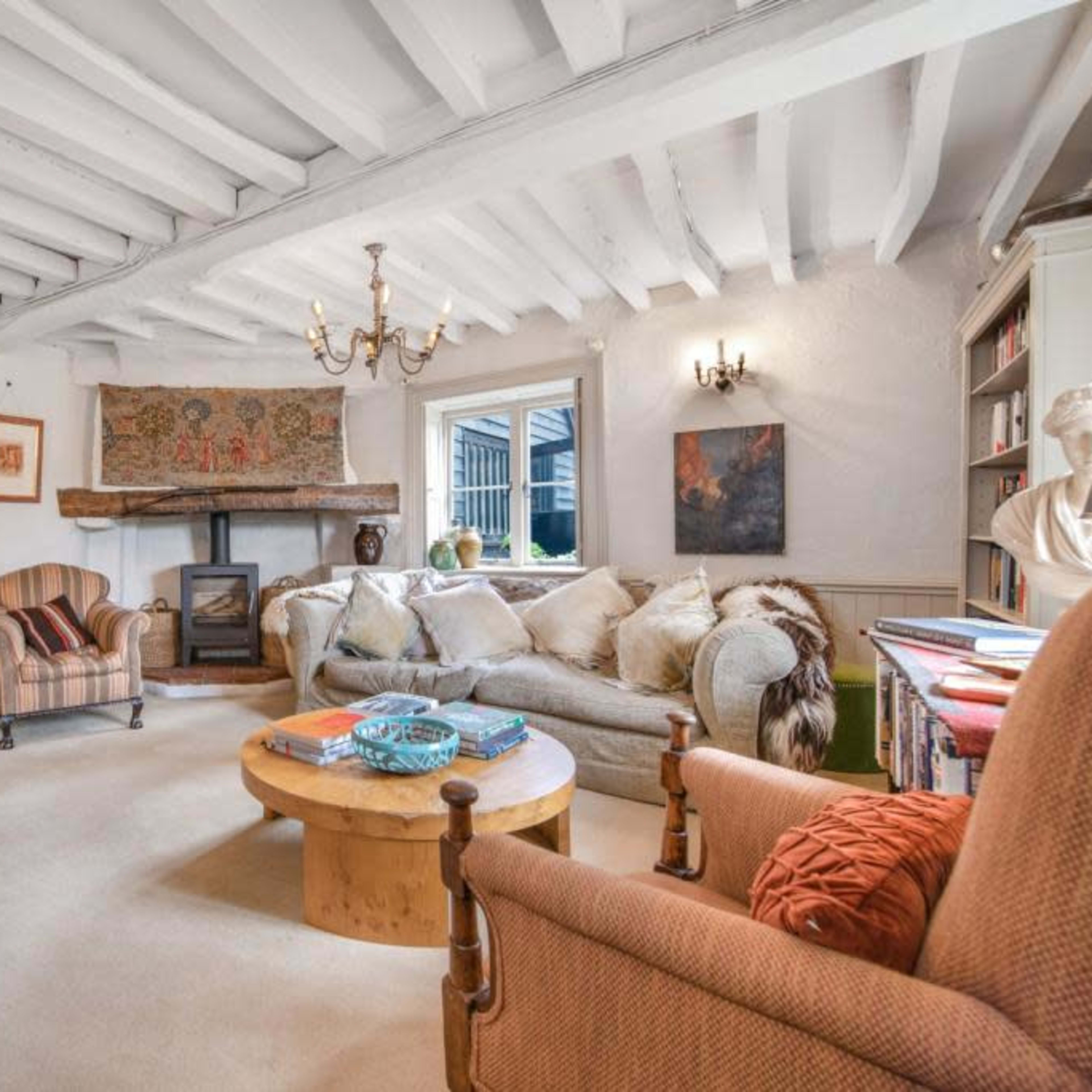 A cozy living room with two striped armchairs, a large sofa, a wooden coffee table, a fireplace, and exposed wooden beams on the ceiling.
