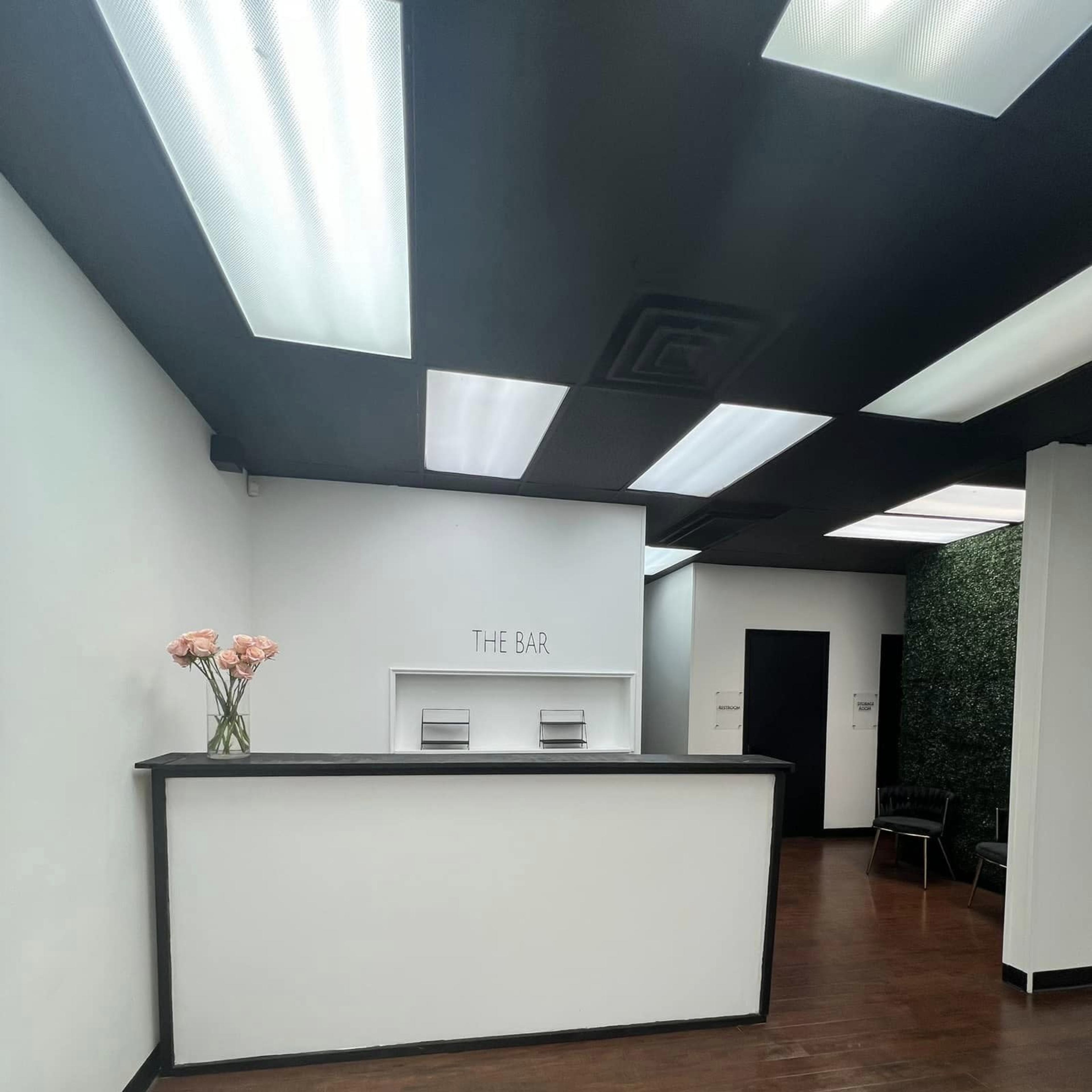 A modern reception area features a sleek black and white design with a floral arrangement on the counter and greenery on one wall.