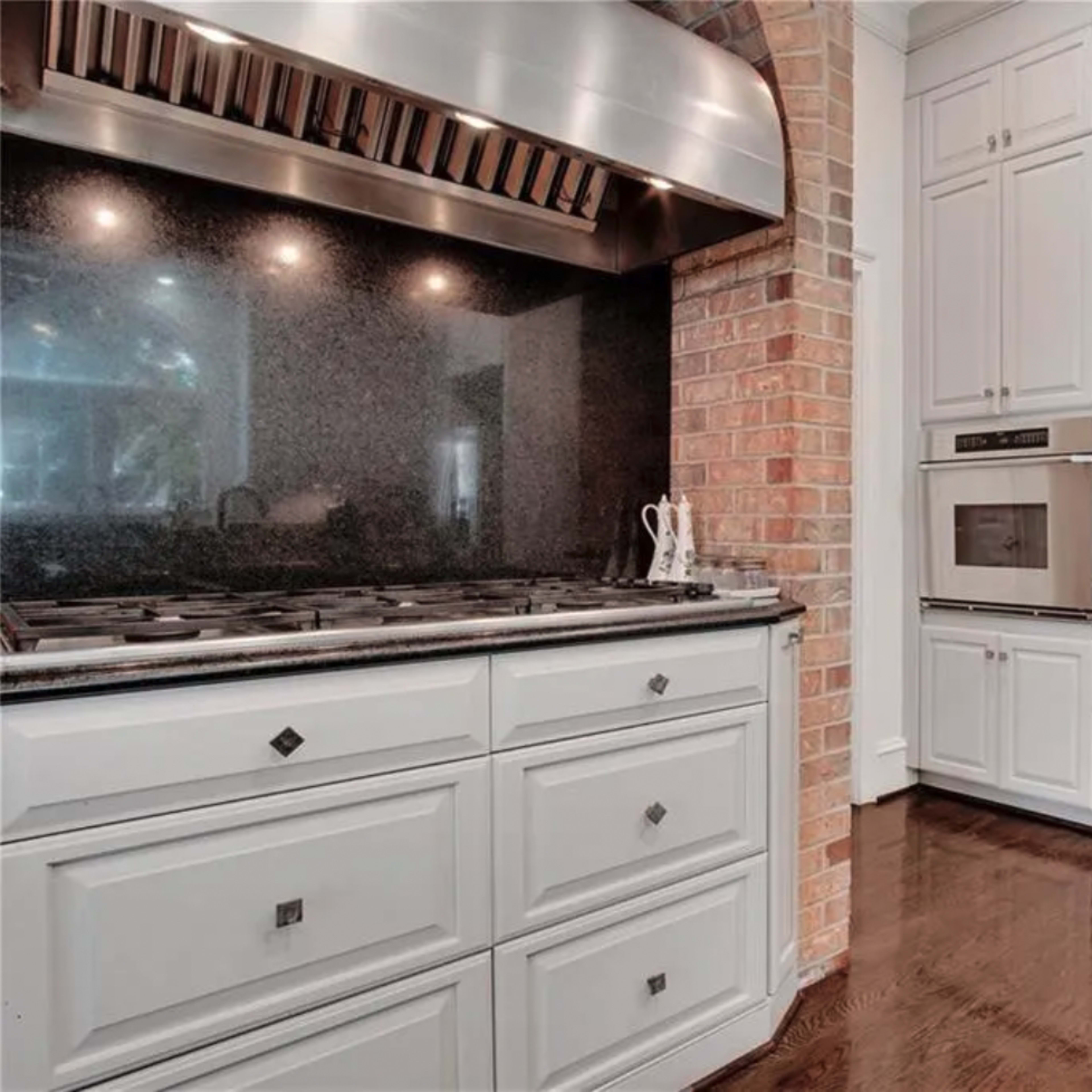 A kitchen with a stainless steel hood above a gas stove, black granite countertops, and white cabinetry containing built-in appliances.