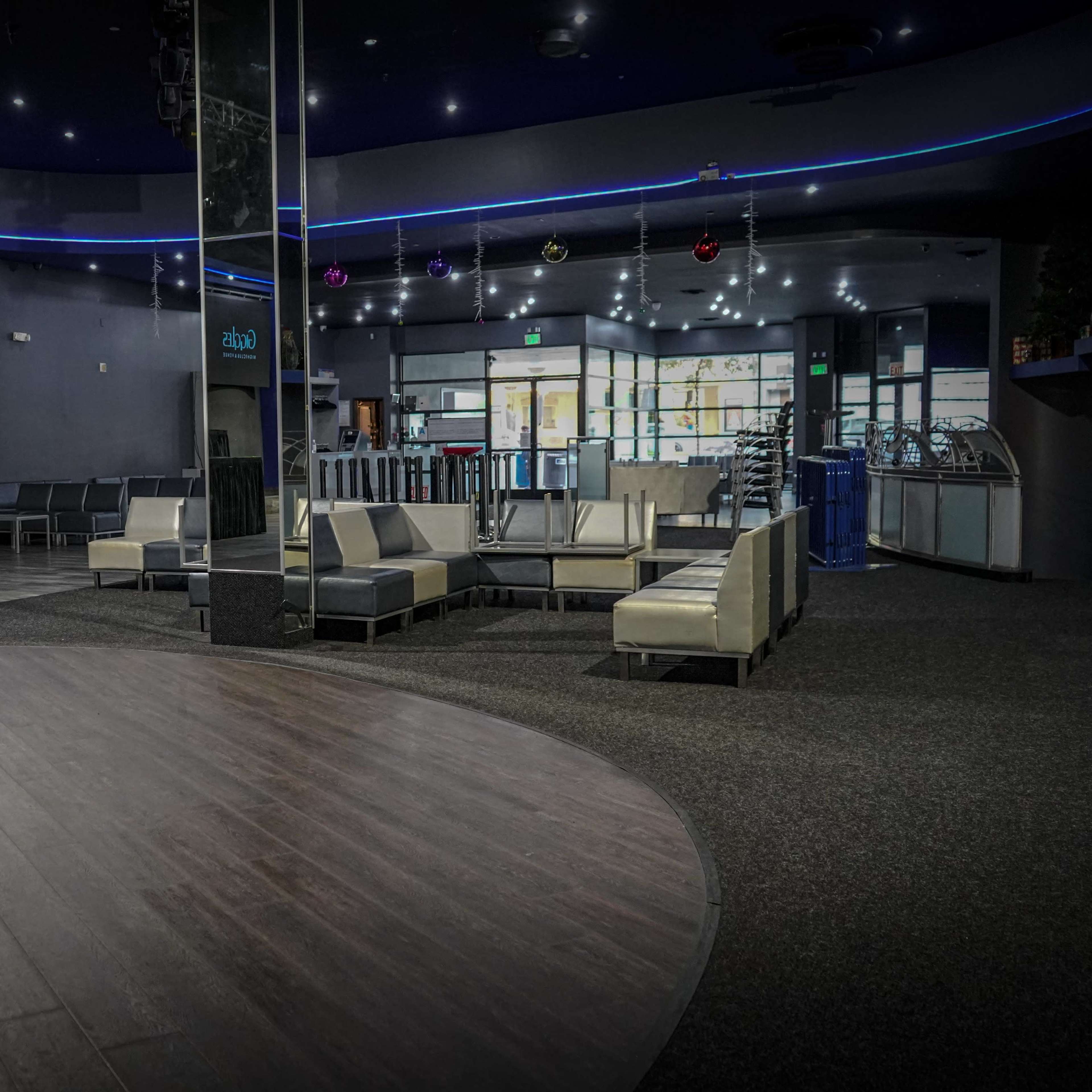A spacious, dimly lit lounge area with modern seating and a large circular wooden section on the floor.