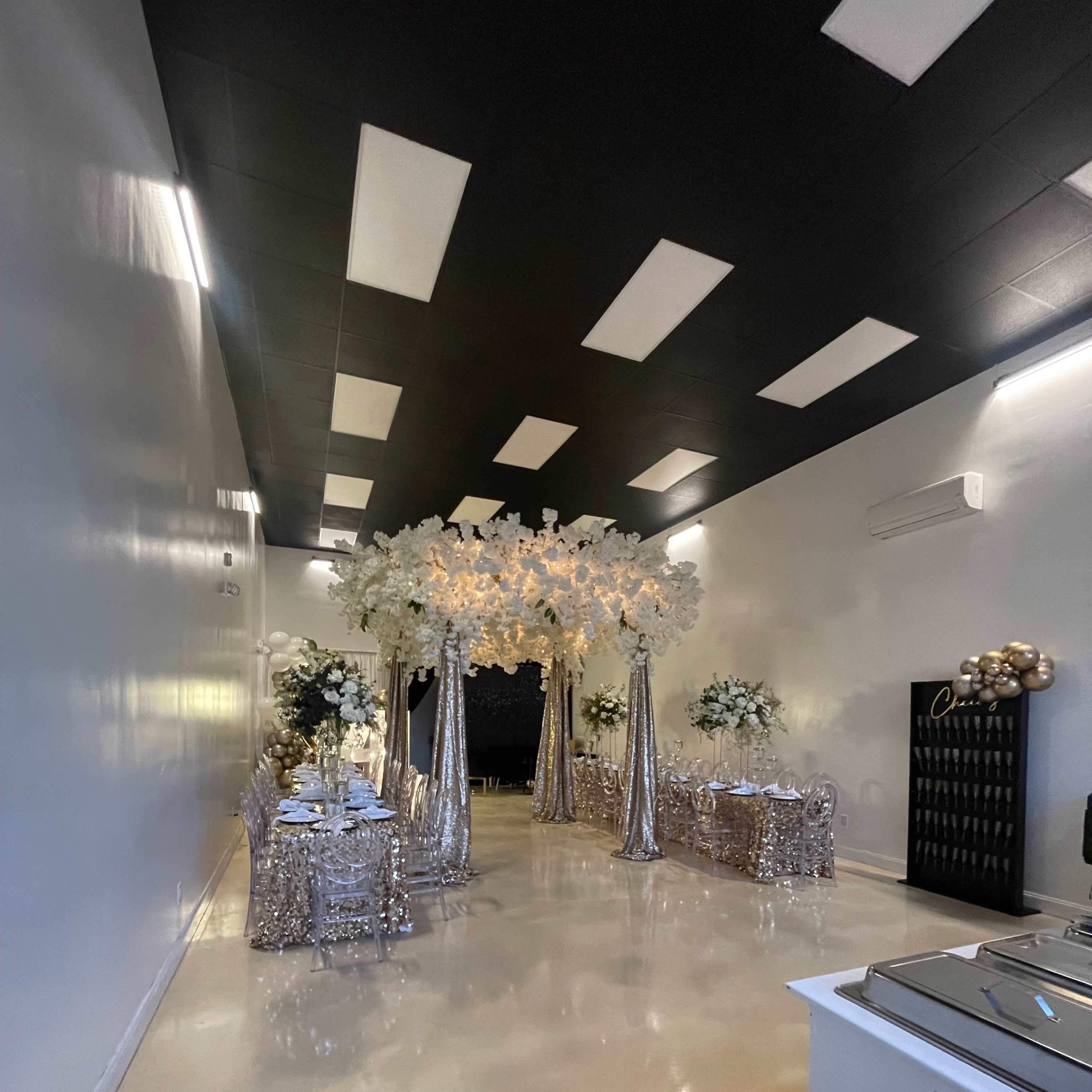 A decorated event space with tables covered in shimmering tablecloths and an elaborate floral arrangement on display.