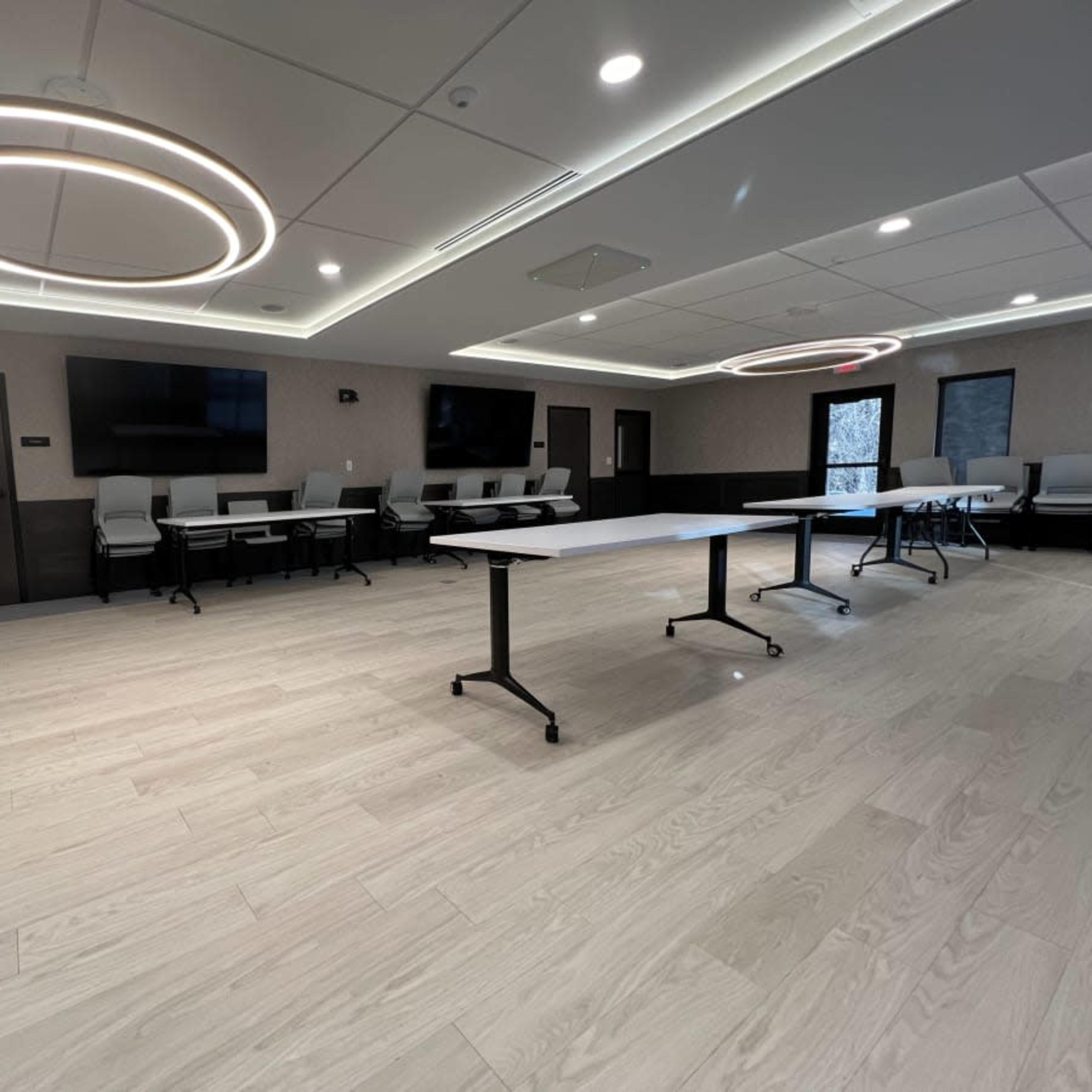 A modern conference room featuring light wood flooring, sleek tables, and circular ceiling lights.