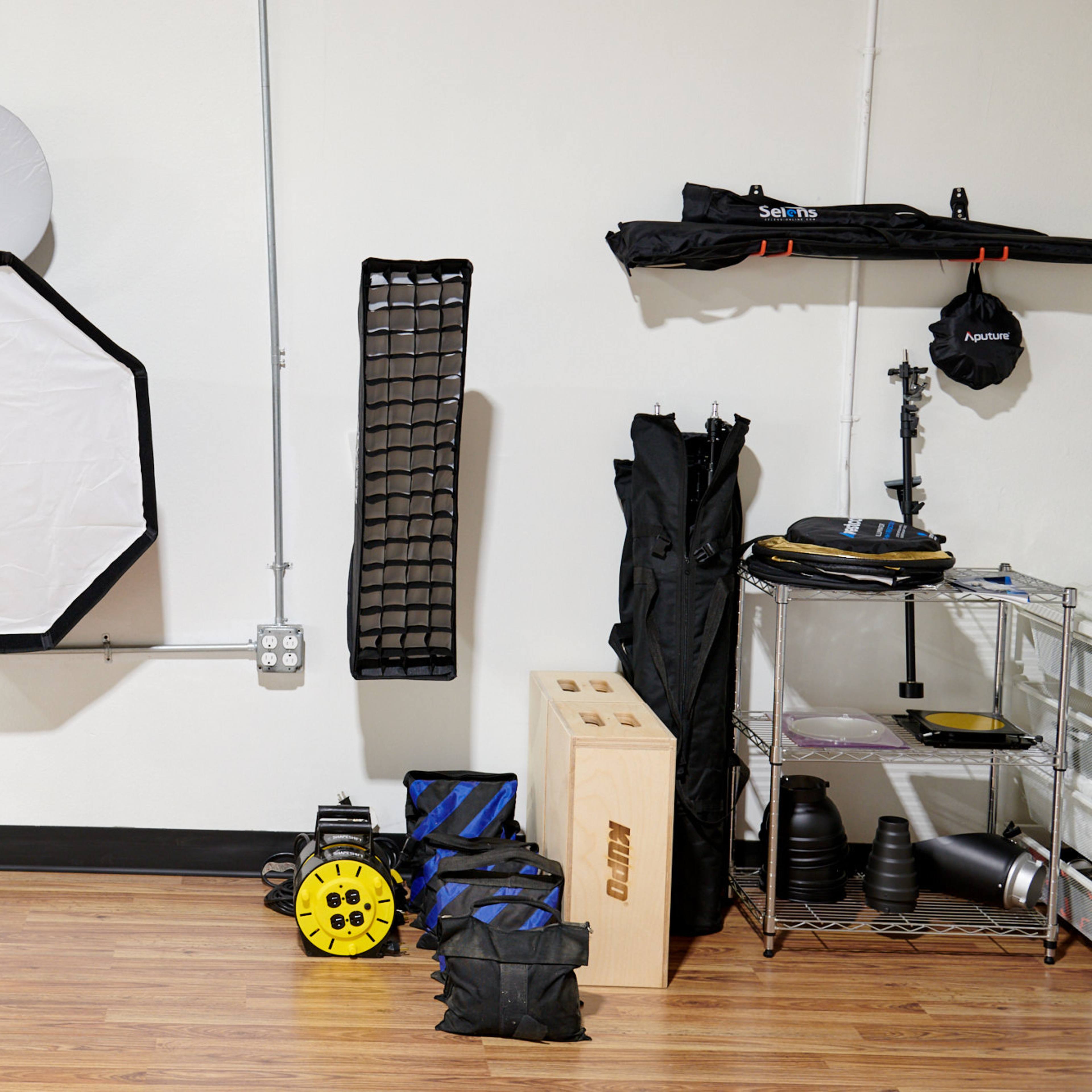 A workspace with various photography equipment, including a large softbox, a grid panel, and storage containers, arranged against a plain wall.