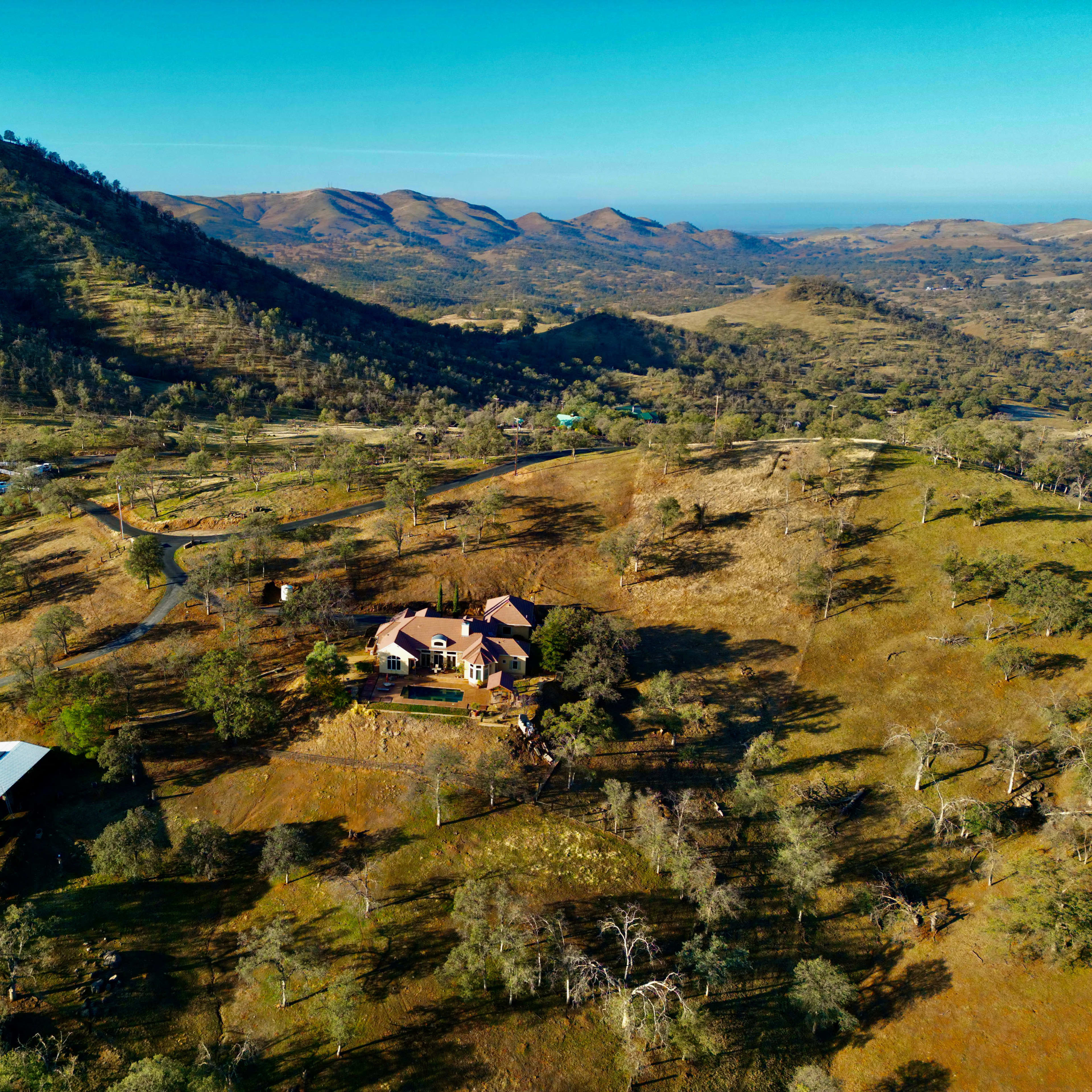 A large house surrounded by rolling hills and scattered trees in a rural landscape.