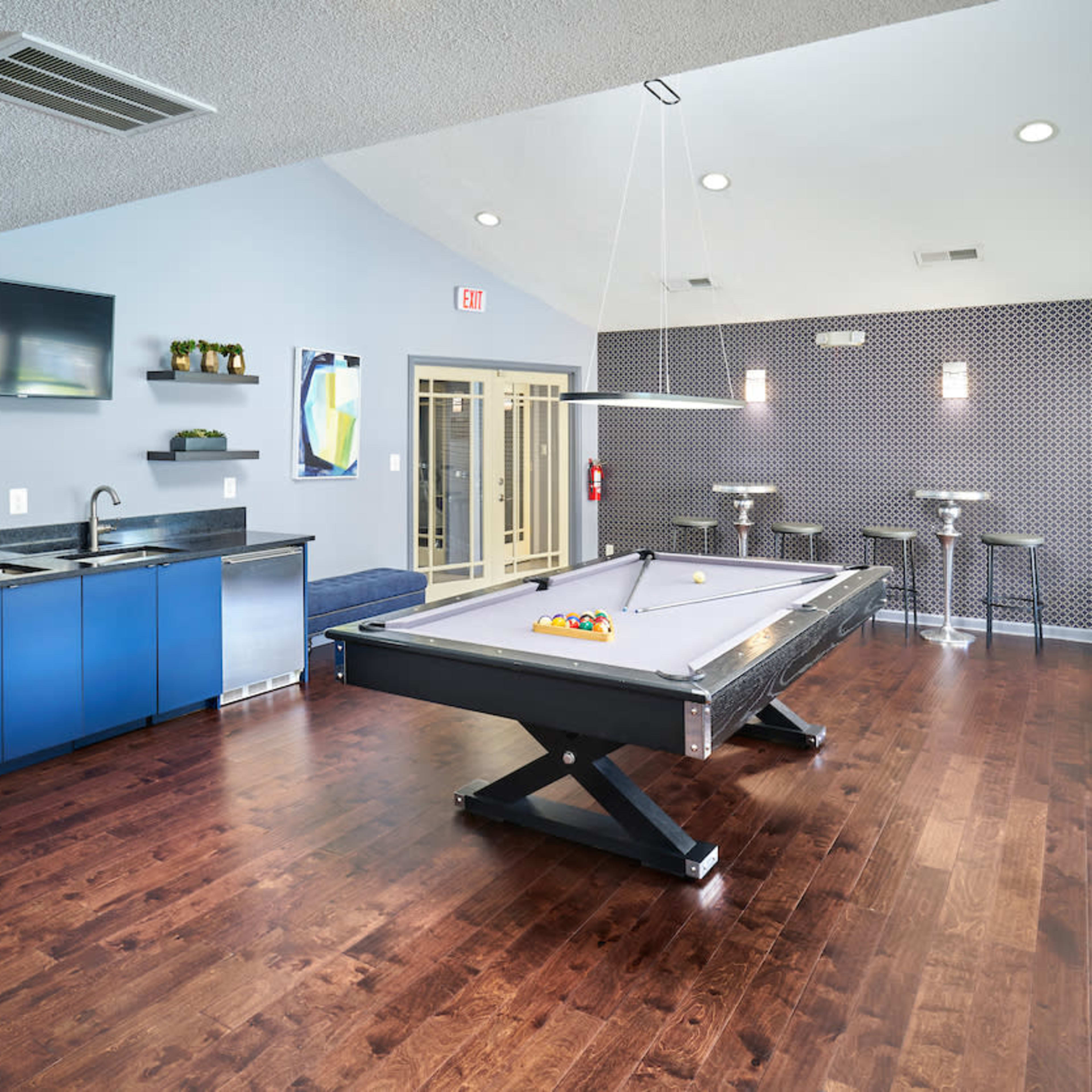 A stylish game room featuring a pool table, a kitchenette with a coffee machine, and seating along the walls.