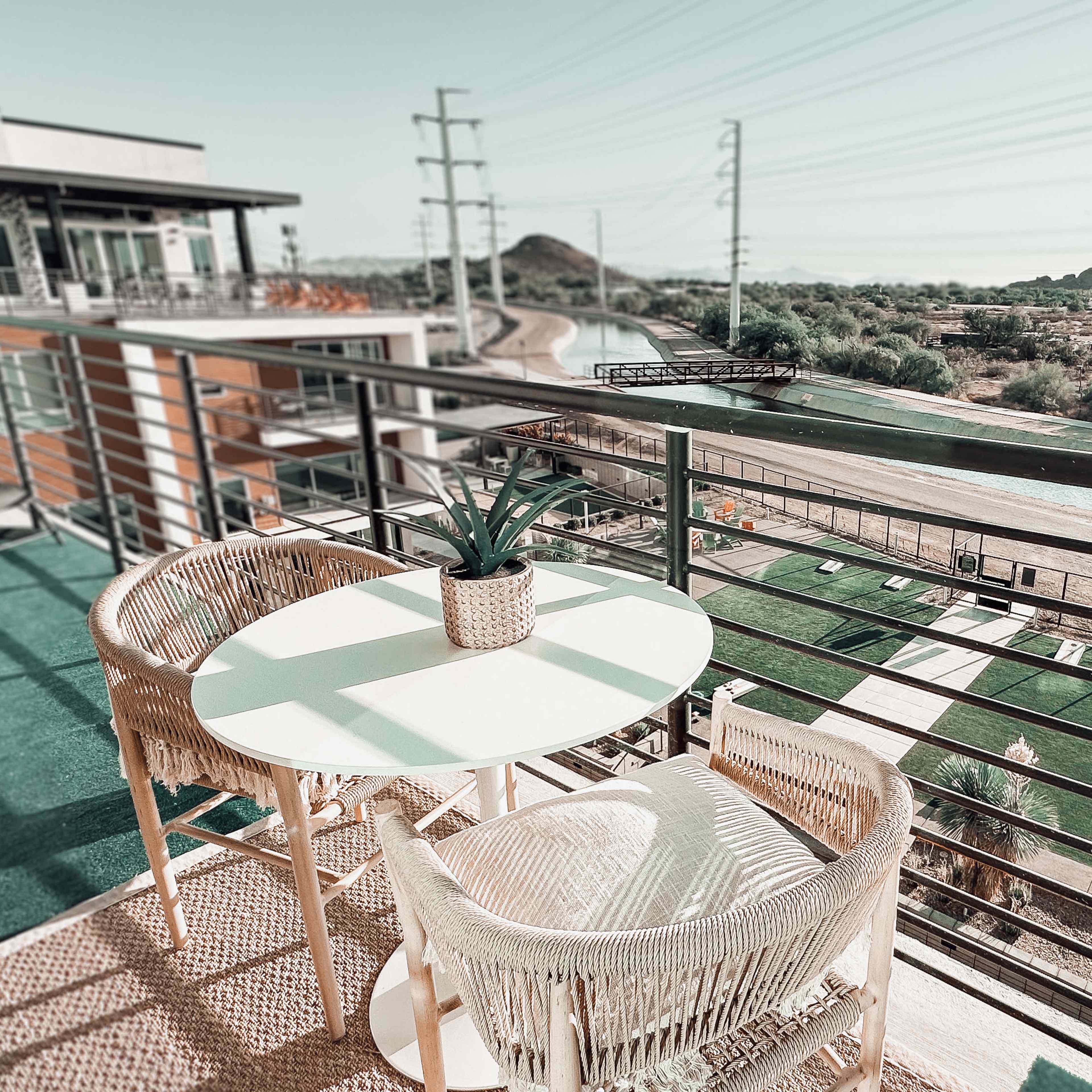 A balcony features a small round table and two chairs, overlooking a scenic landscape with power lines and distant mountains.