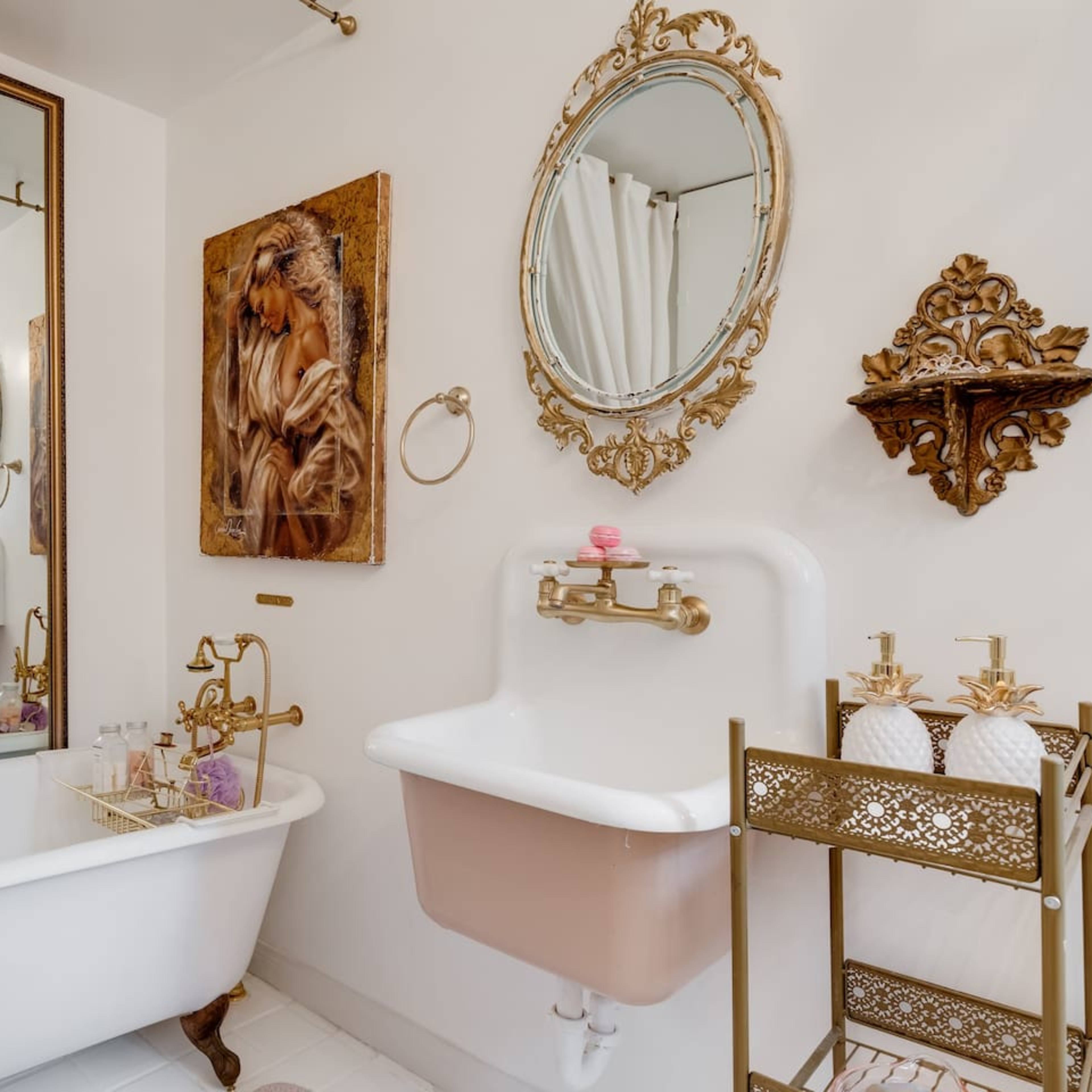 The bathroom features a vintage clawfoot tub, elegant mirrors, ornate wall decor, and a decorative towel rack.