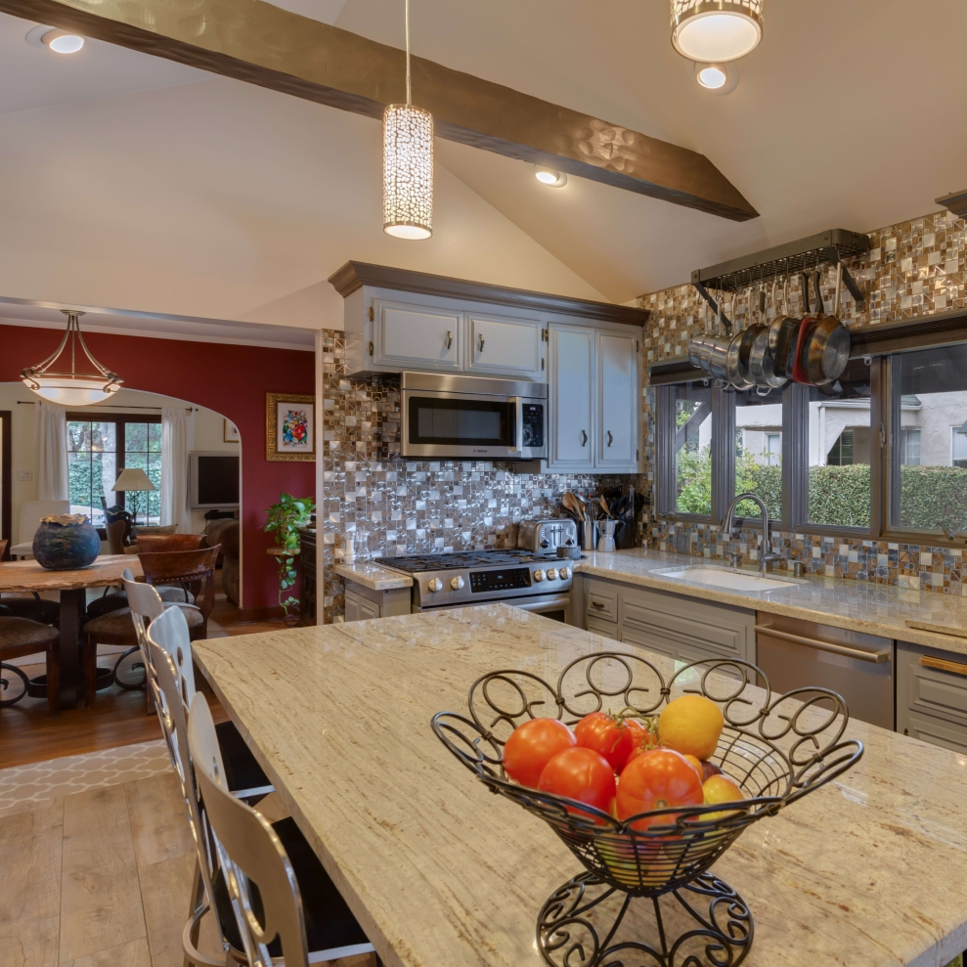 A modern kitchen with a granite island countertop, stainless steel appliances, and a bowl of colorful fruit at the center.