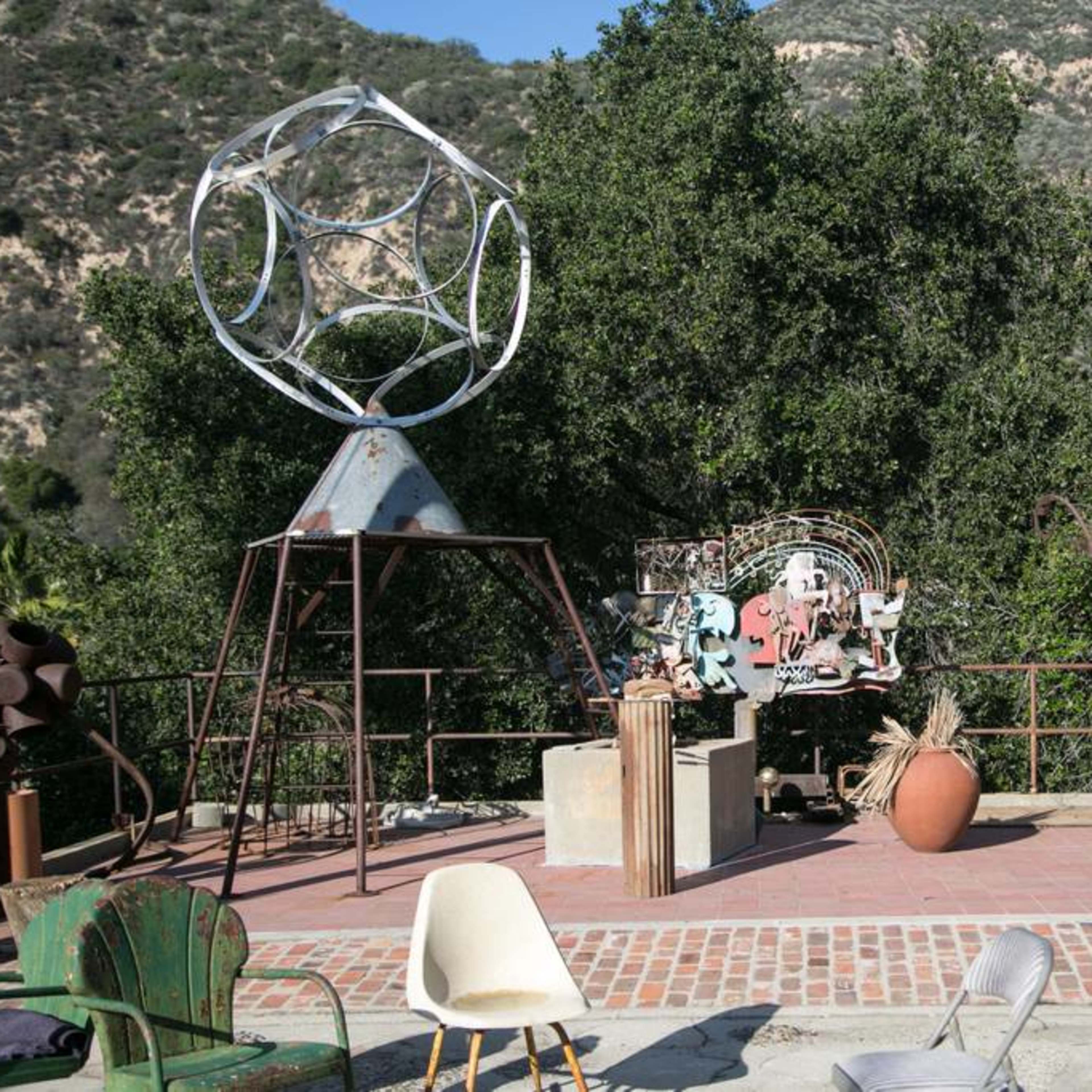 An outdoor sculpture garden featuring various metal sculptures and a backdrop of green hills.