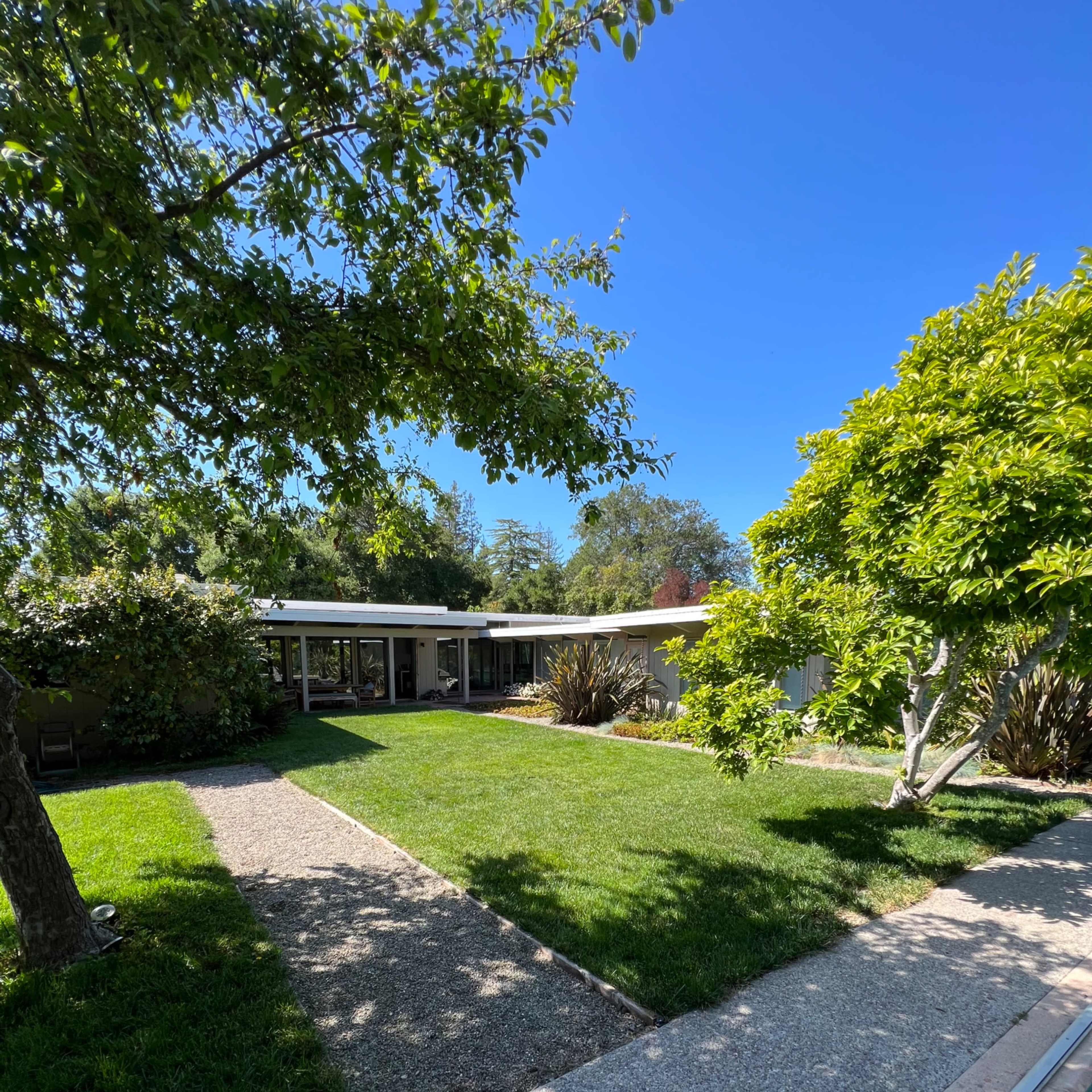 A modern house with a flat roof and large windows sits beside a swimming pool, surrounded by well-maintained grass and trees.