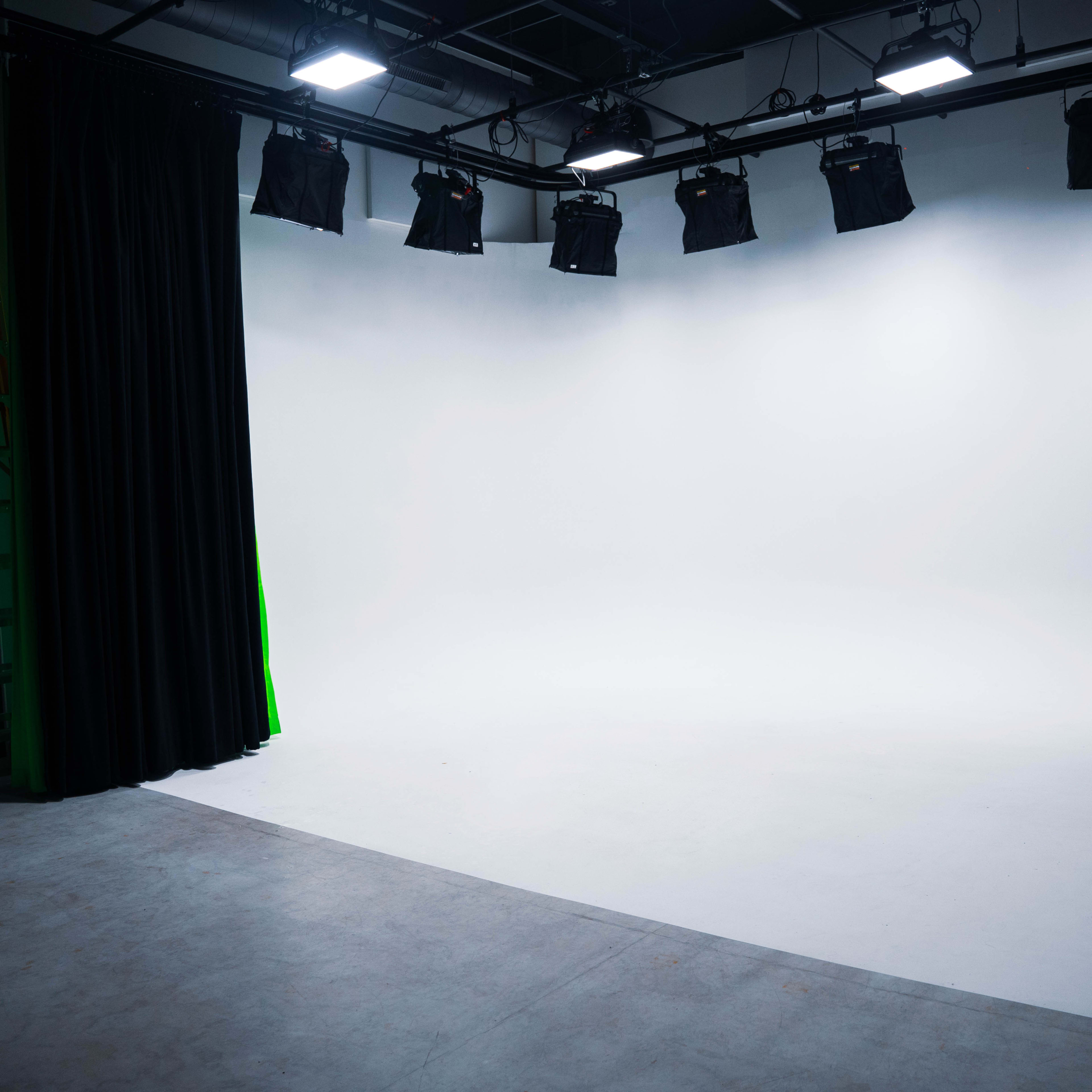 A blank photography studio with a white backdrop, lighting fixtures, and a large black curtain.