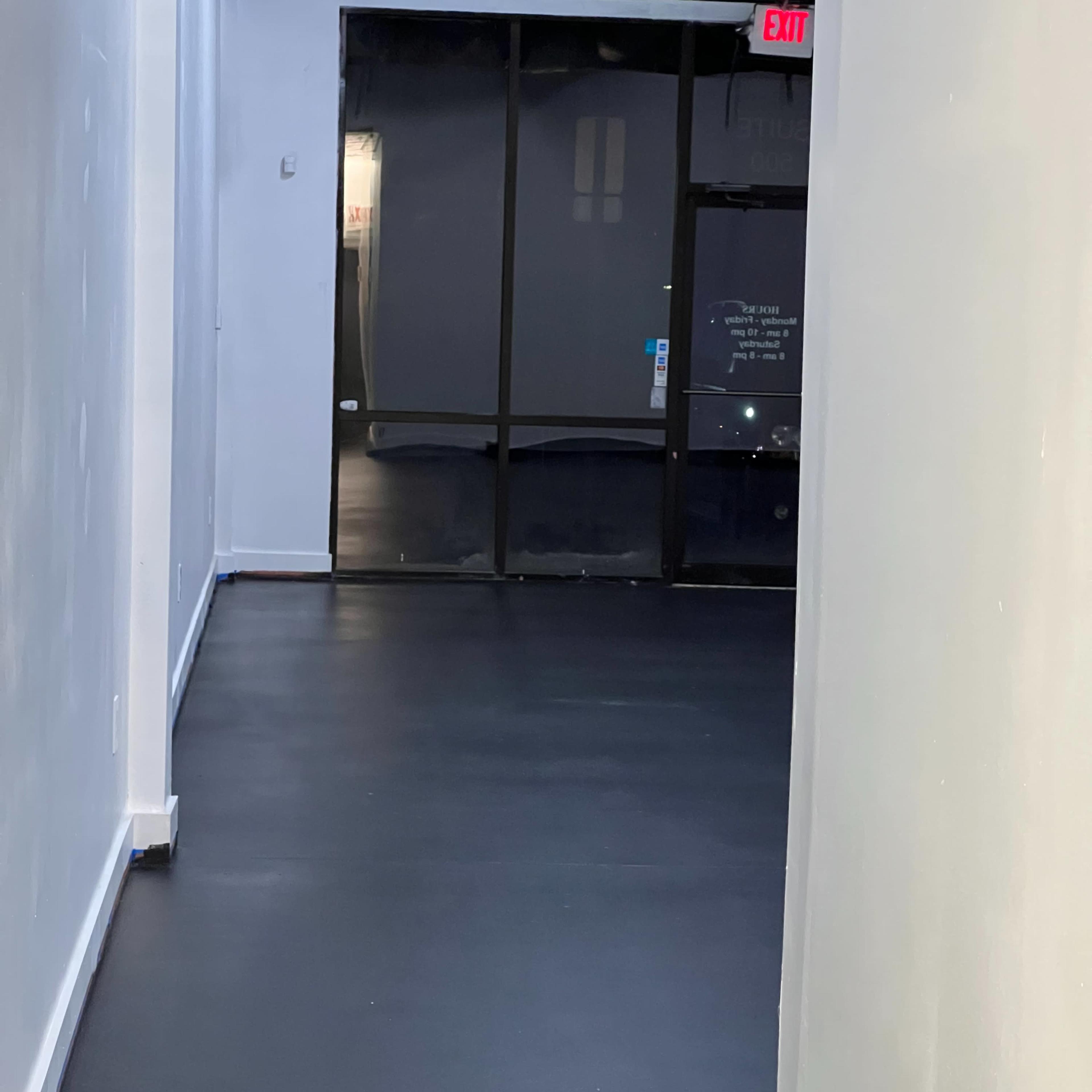 A narrow corridor with black flooring leading to a glass door at the far end.