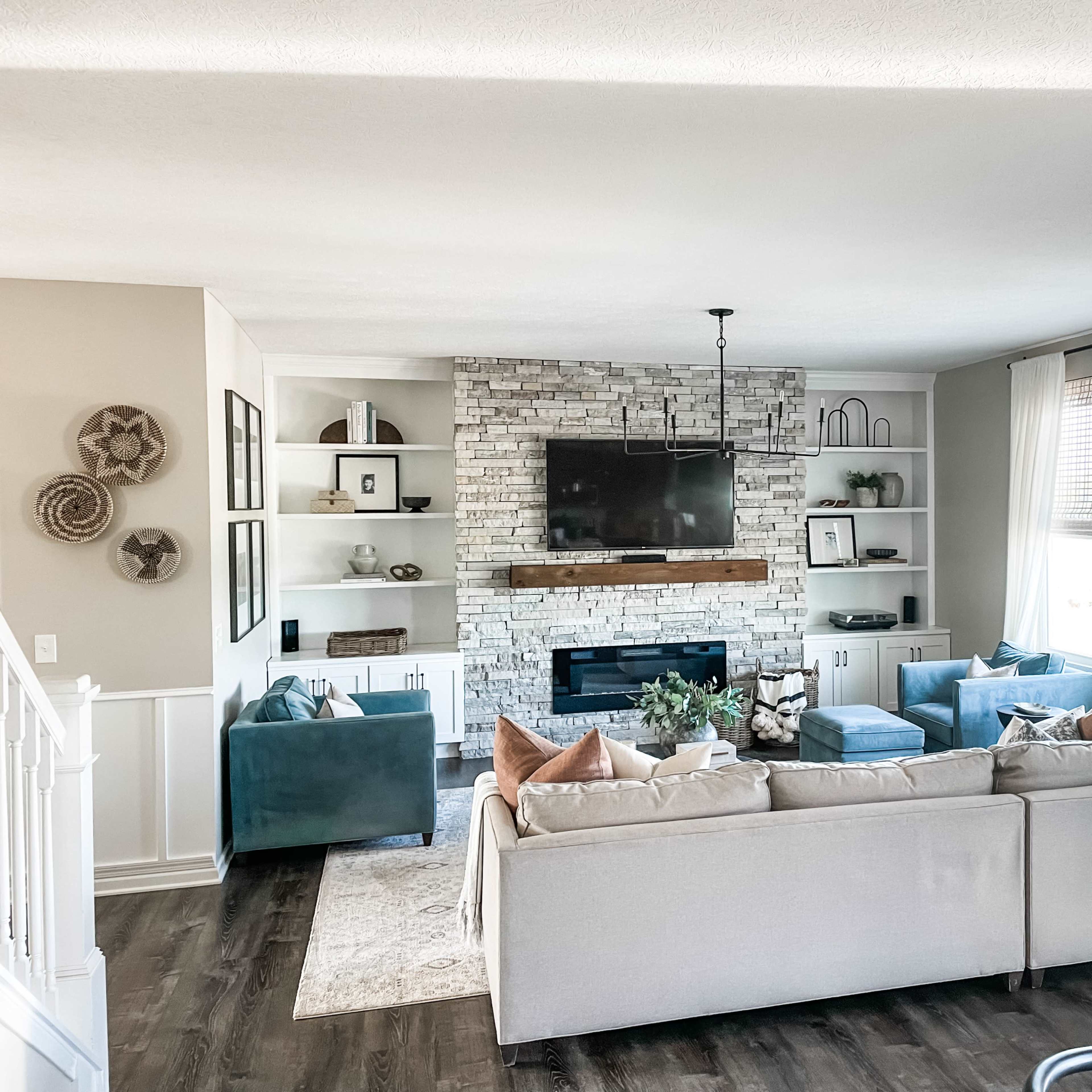 The living room features a stone fireplace, modern furniture, and large windows allowing natural light to fill the space.