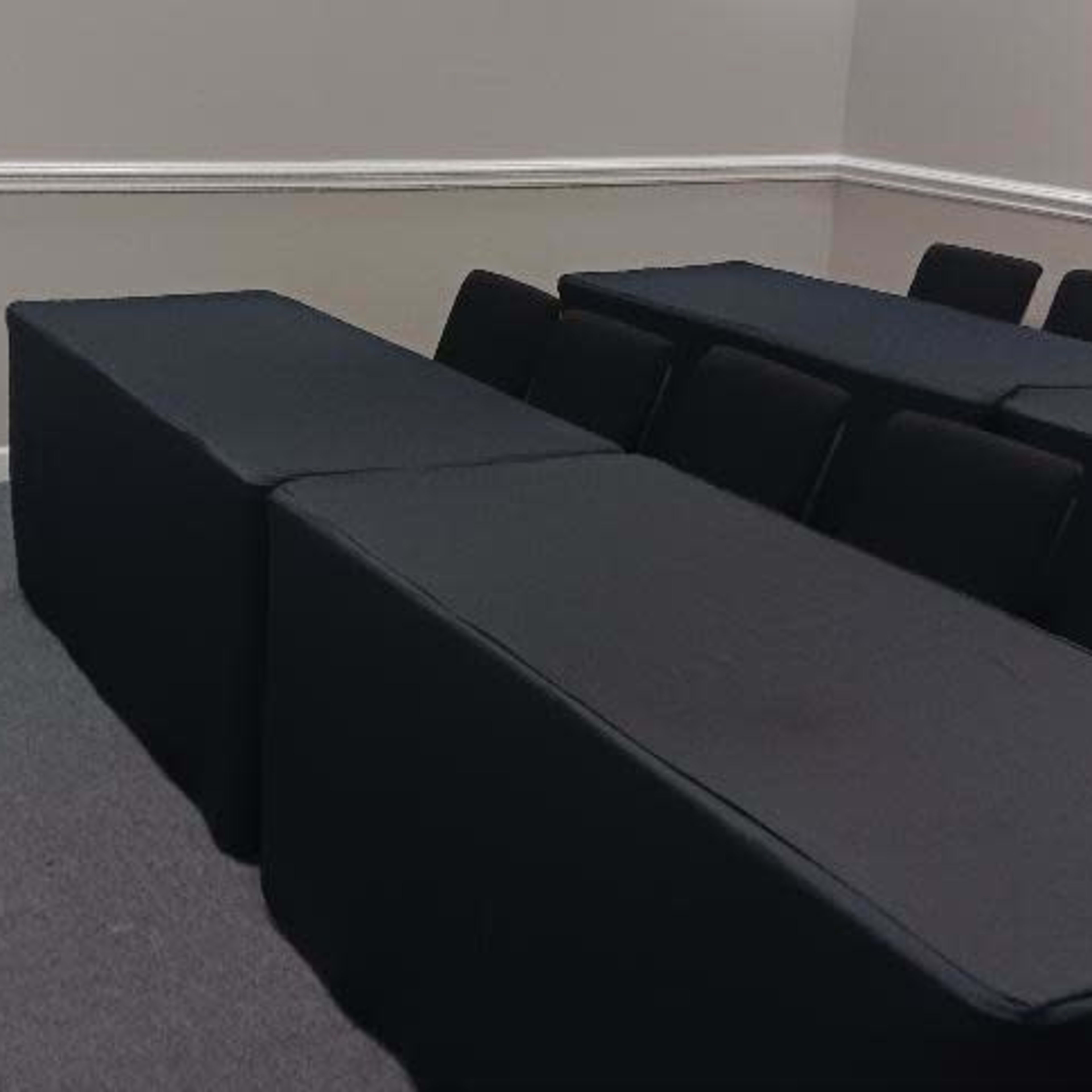 A conference room with two long tables covered in black cloth and several chairs arranged behind them, alongside a white podium at the front.