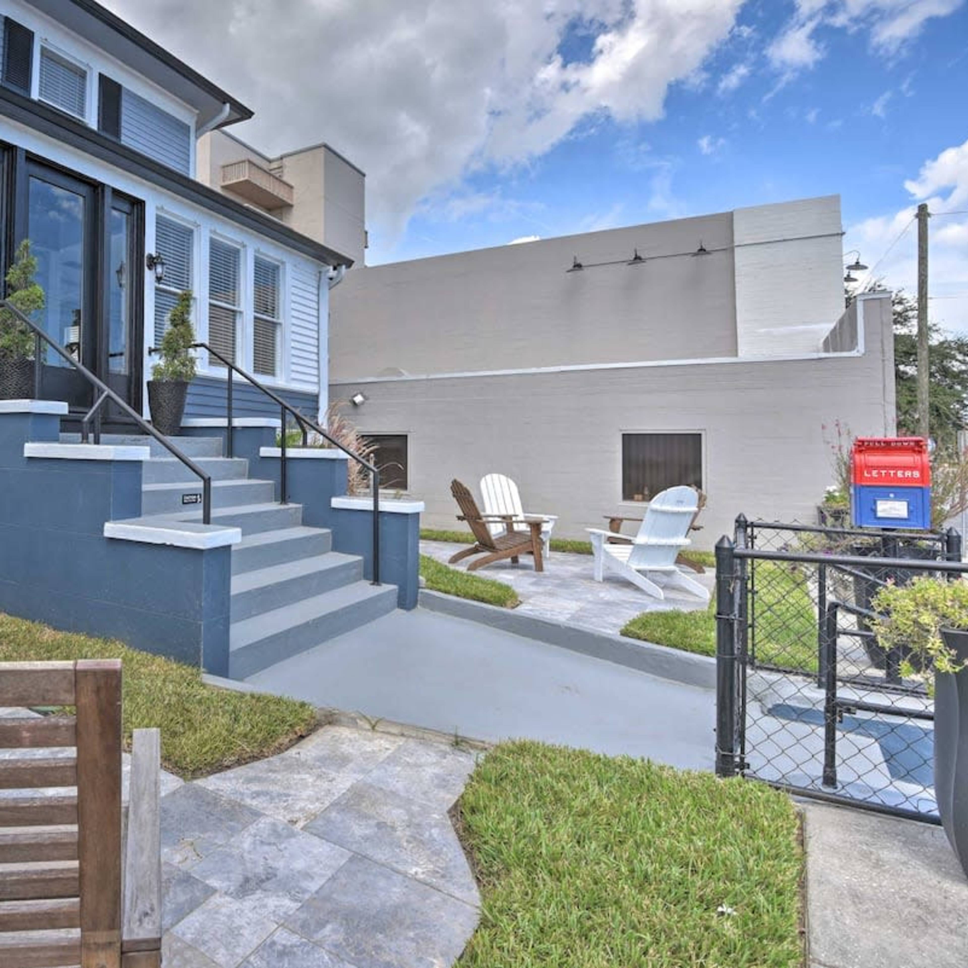 A blue house with steps leading up to a patio area featuring wooden chairs and a grassy lawn.