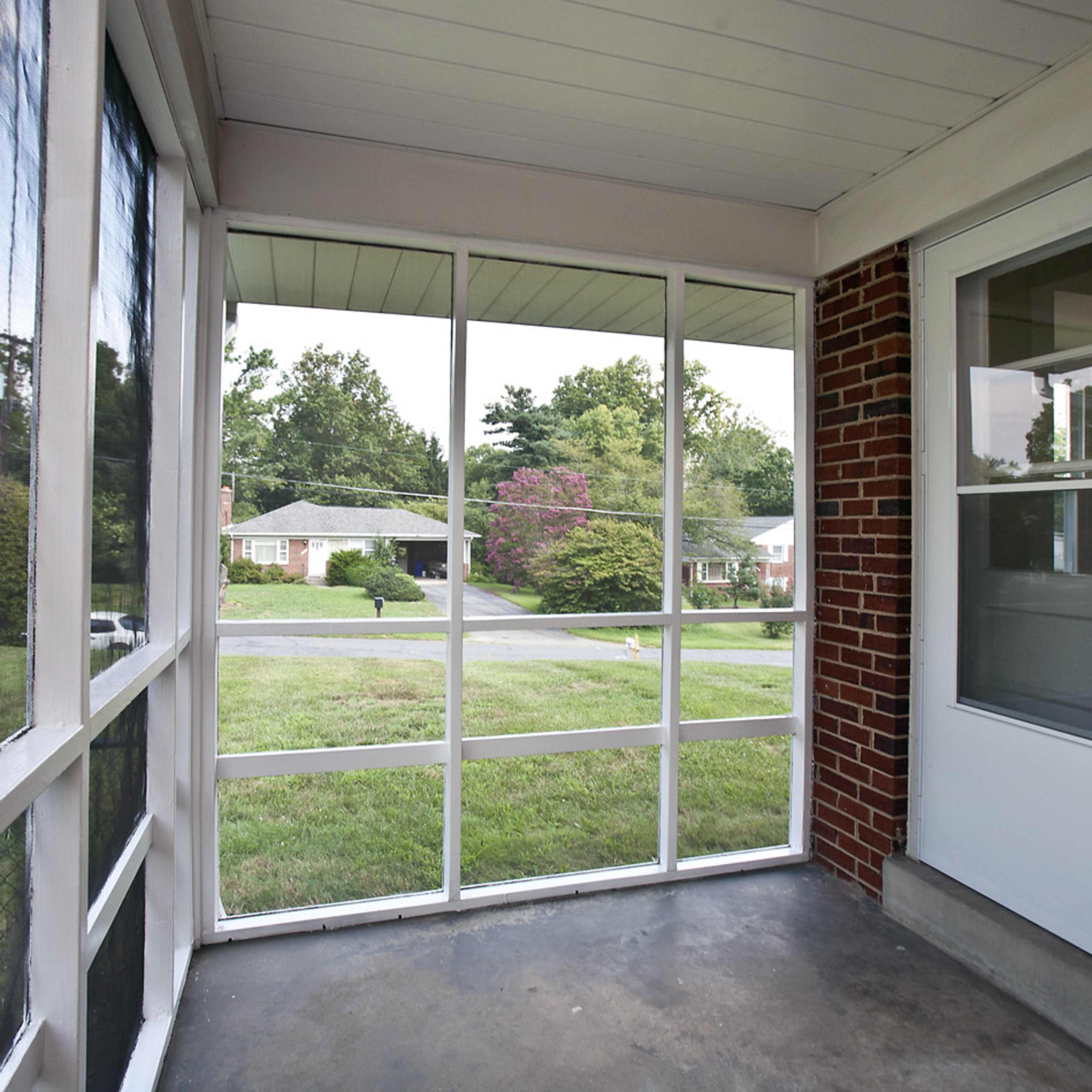 A screened porch with brick walls and a view of a grassy yard and houses outside.