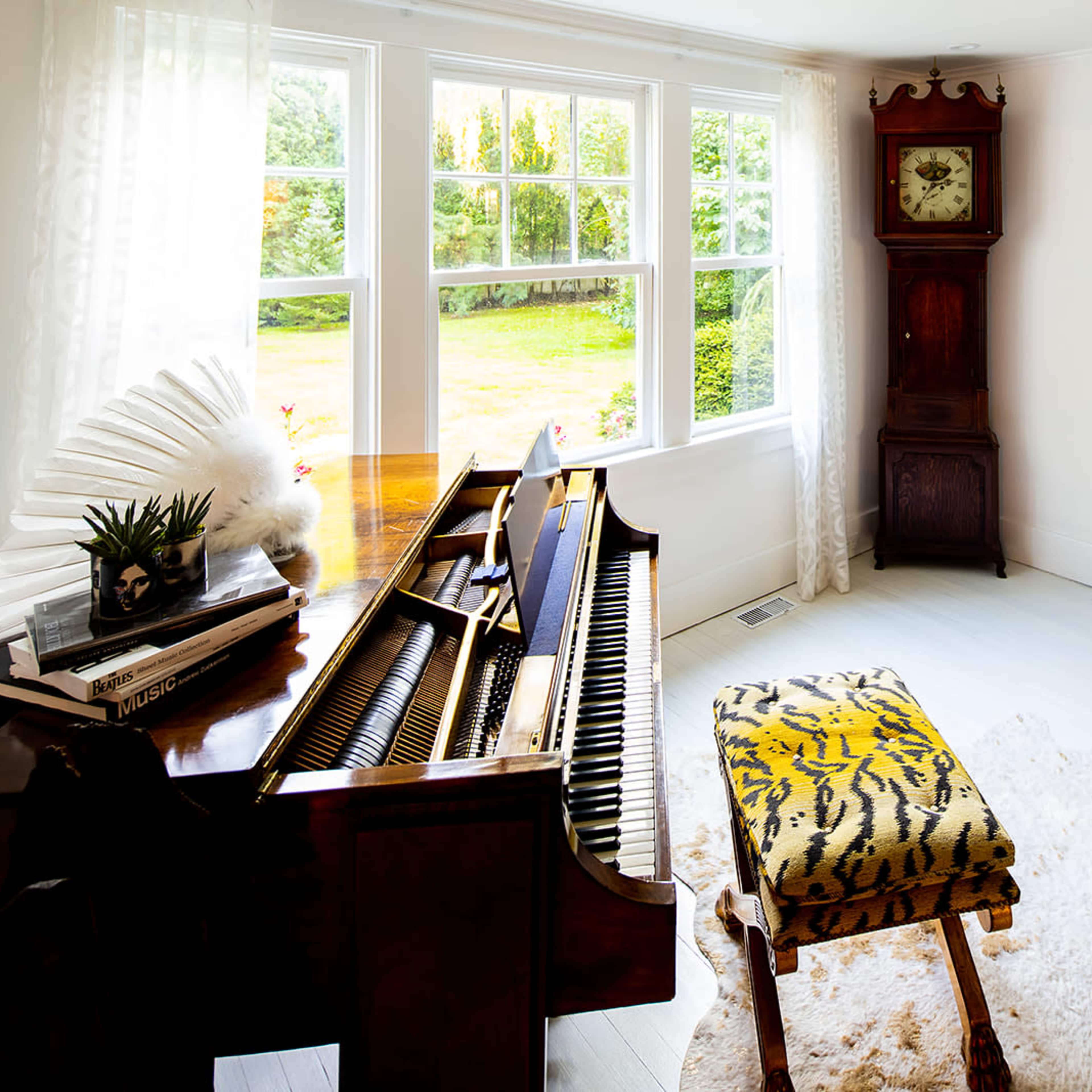 A grand piano is positioned beside a window in a bright room, leading to another area decorated with vibrant furniture and playful accessories.