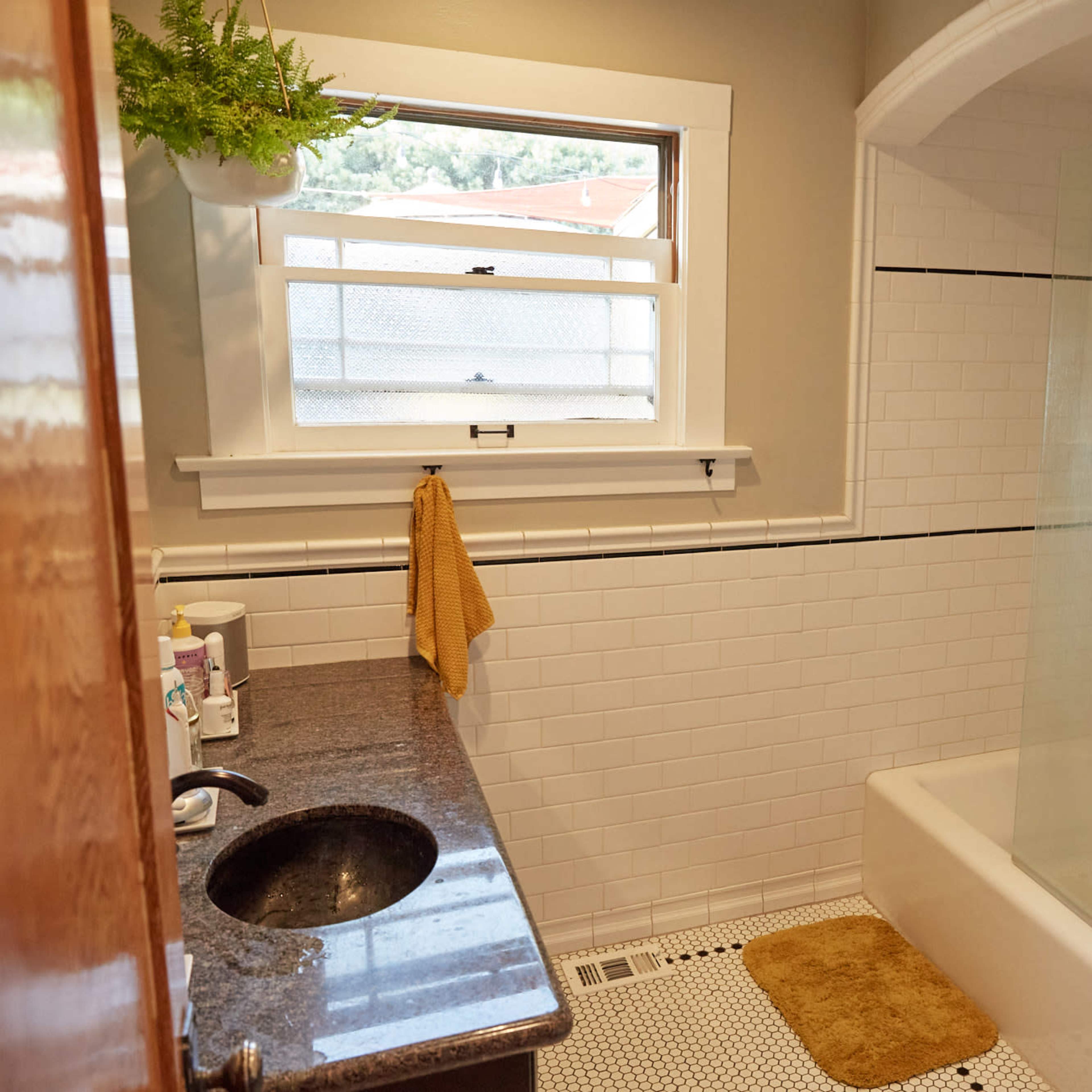 A bathroom with a shower and tub combination, a dark granite counter with a sink, and white tiled walls.