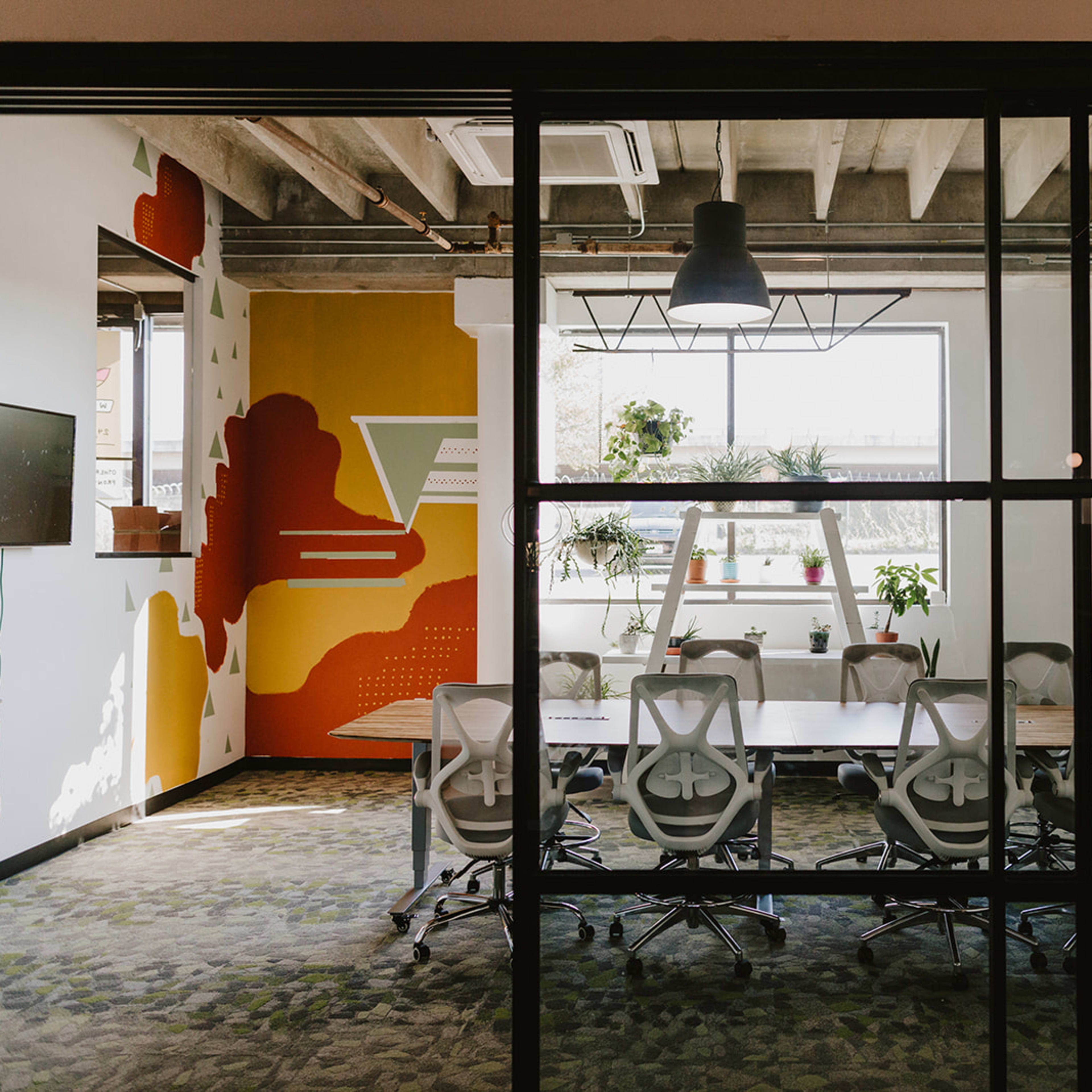 A modern conference room with a large table, several ergonomic chairs, and a colorful accent wall featuring abstract designs.