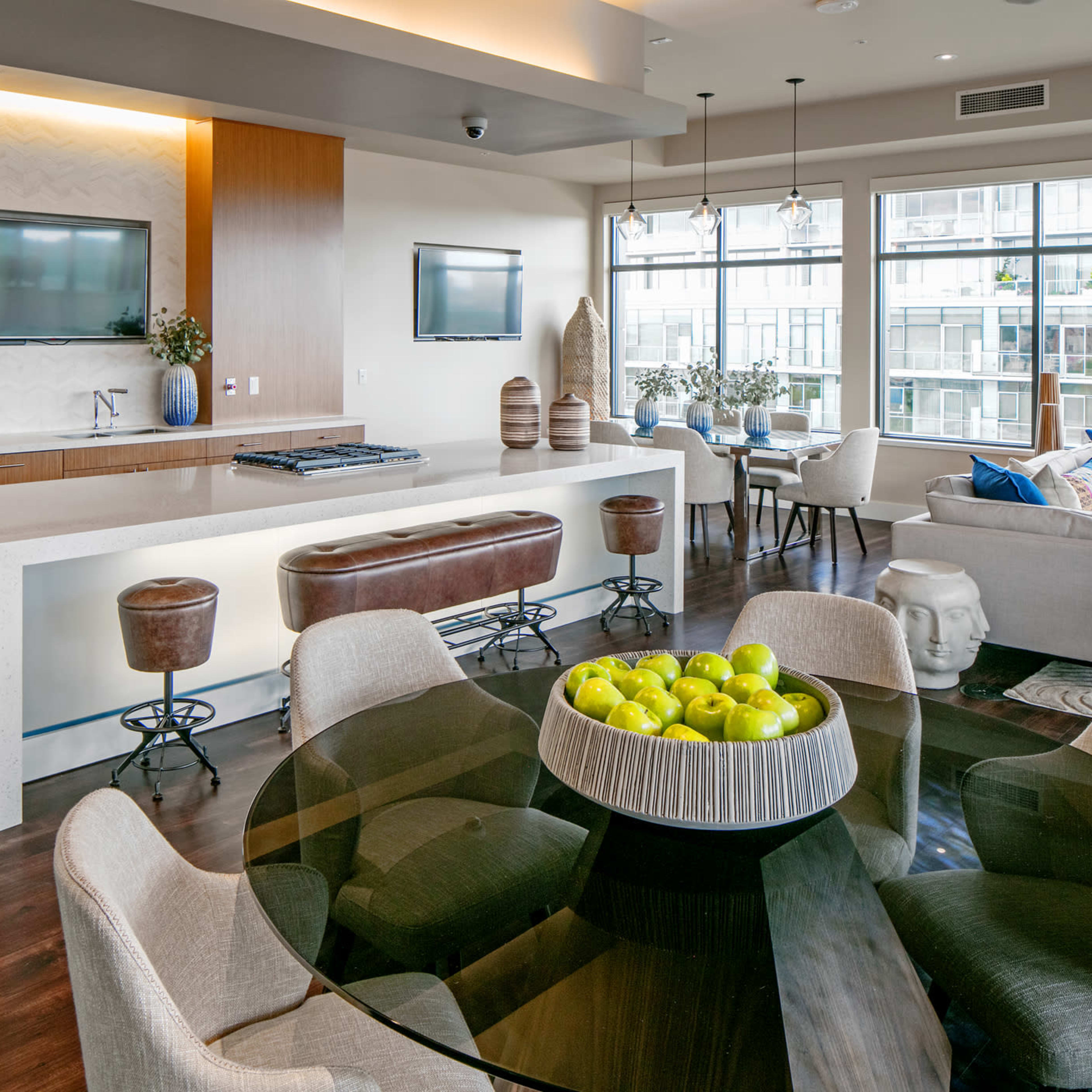 A modern living space featuring a kitchen island, dining table, and a seating area with large windows allowing natural light.