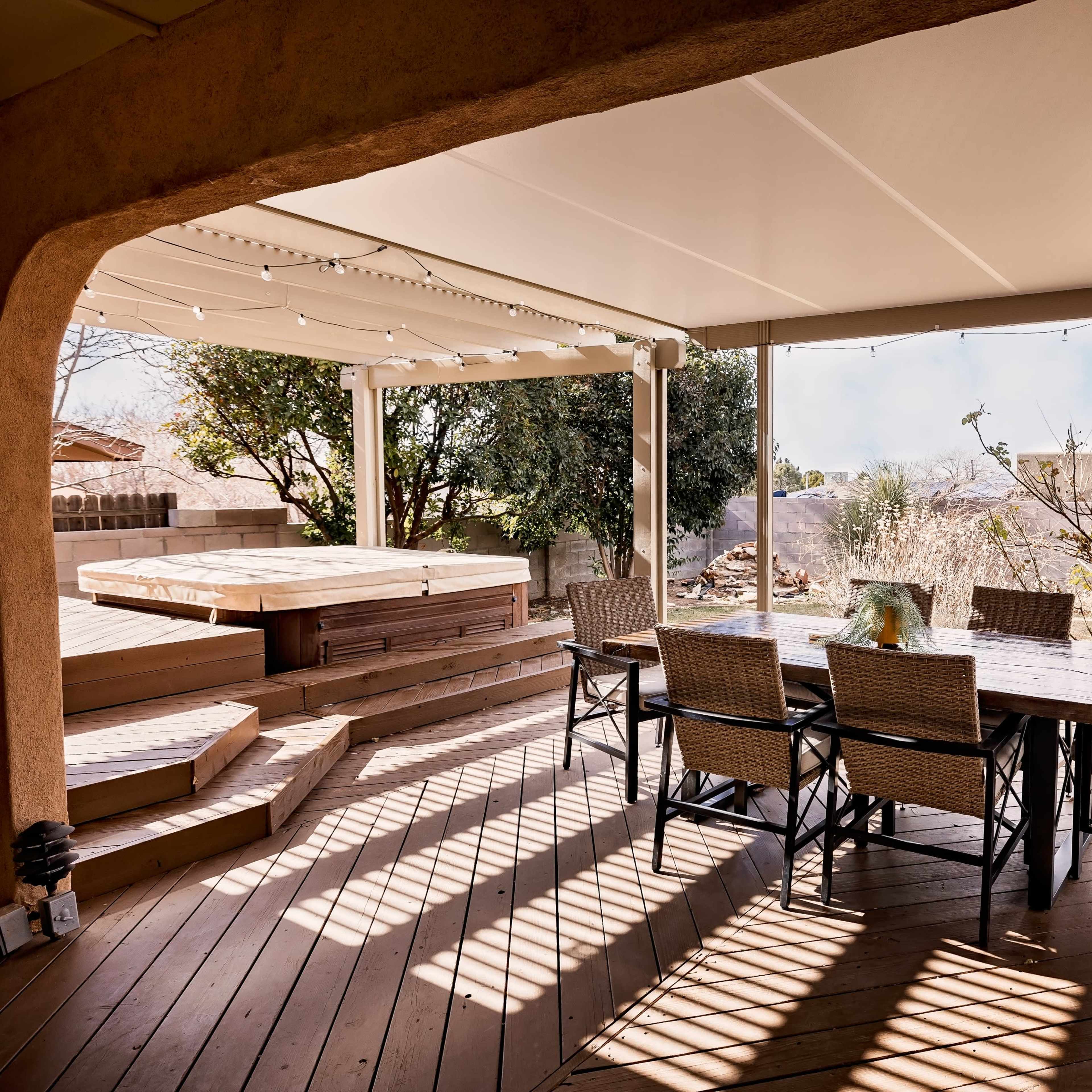 A patio area features a dining table surrounded by chairs, with steps leading to a hot tub and landscaped garden in the background.