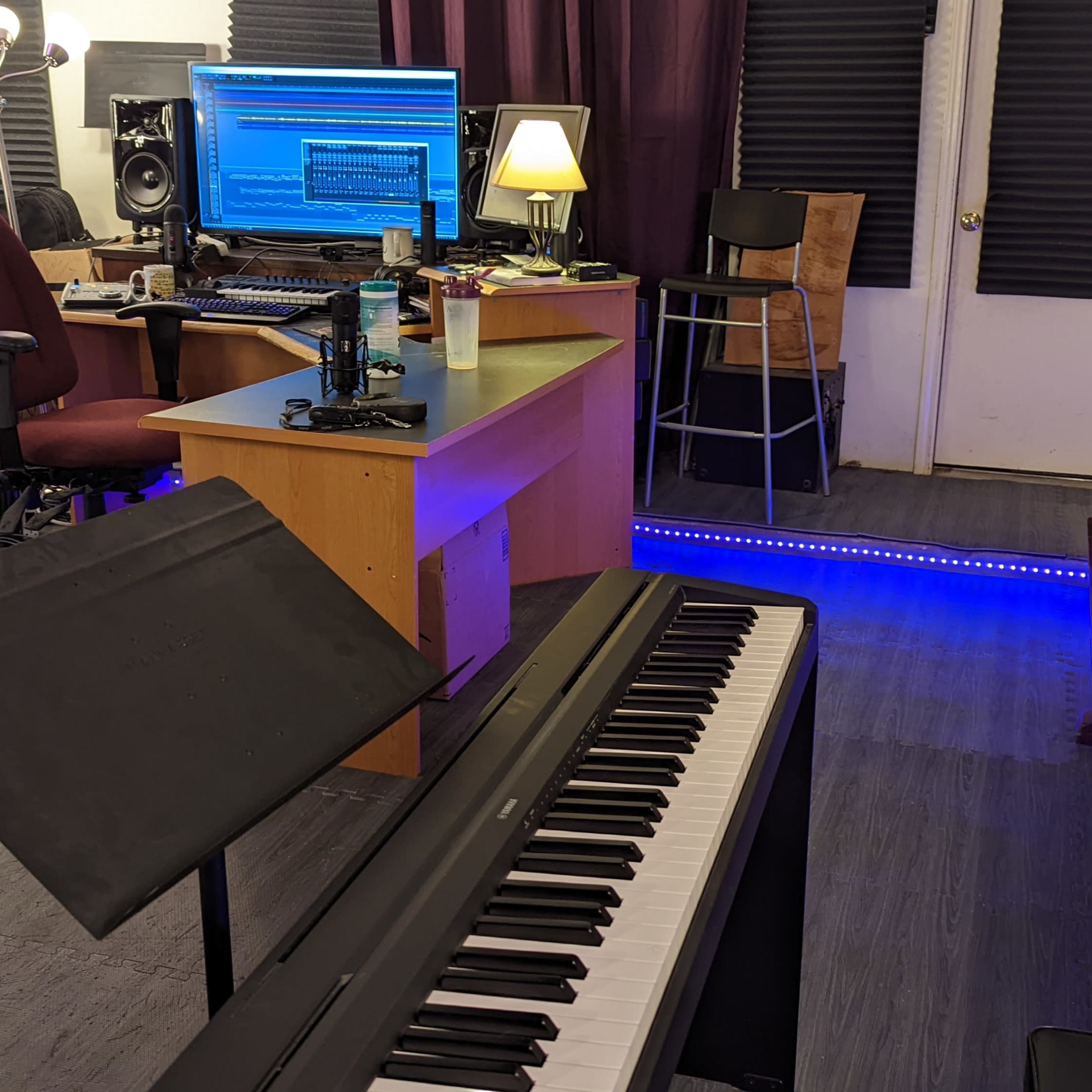 A music studio featuring a digital piano, a desktop computer with music software displayed, and seating arrangements, all illuminated by soft lighting.