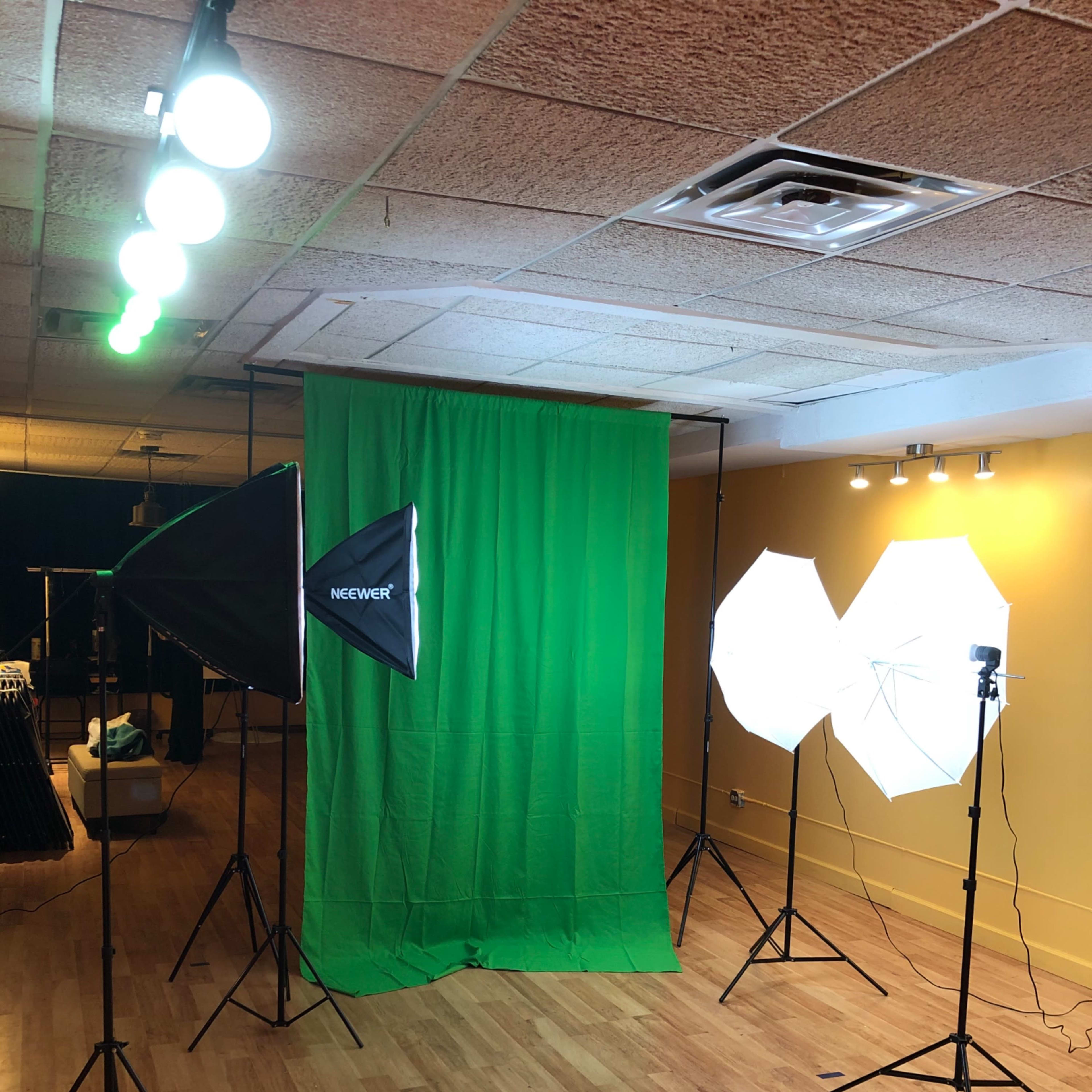 A photography studio setup featuring a green backdrop and several lighting equipment, including softboxes and umbrella lights.