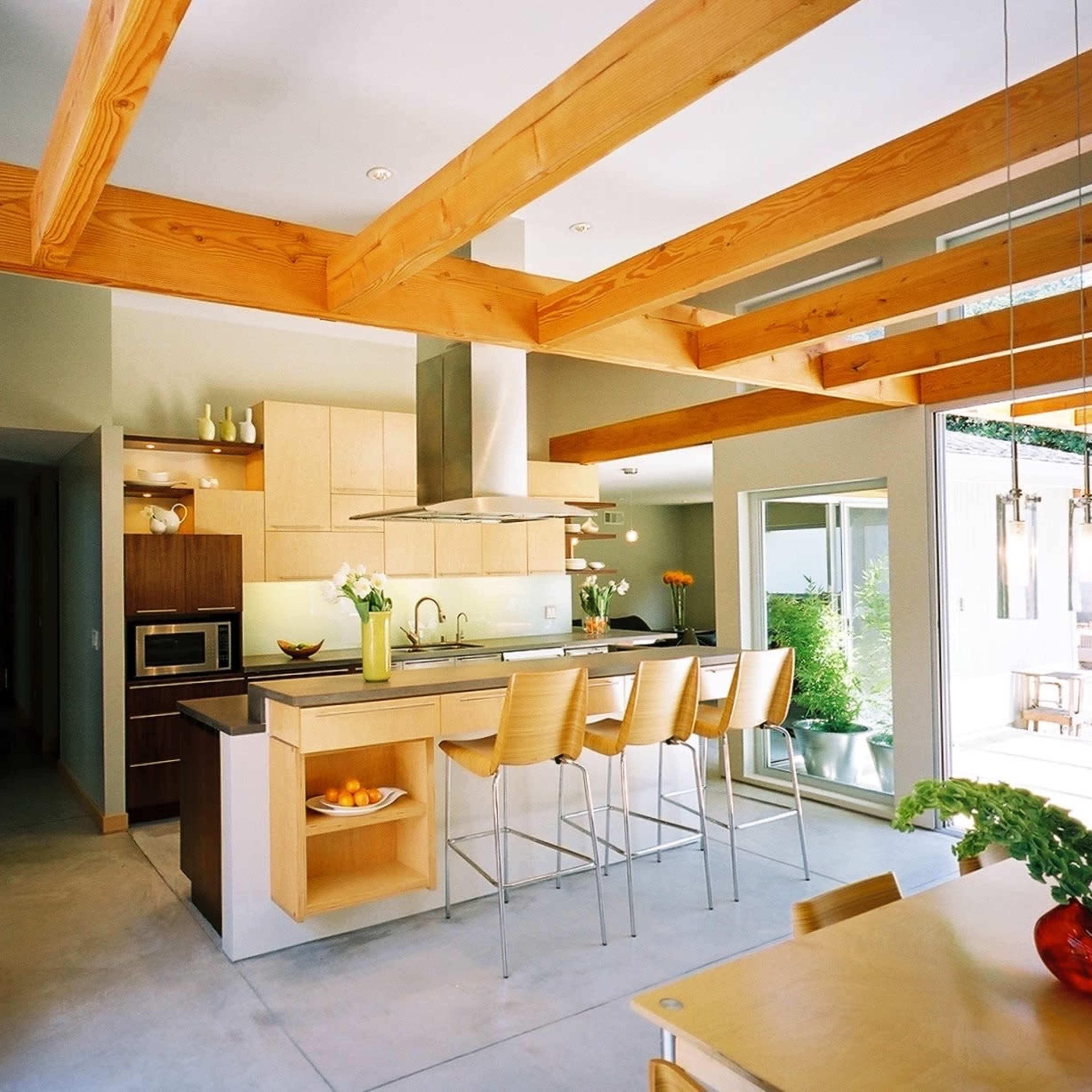 A modern kitchen with wooden beams, light-colored cabinetry, and a central island with bar stools.