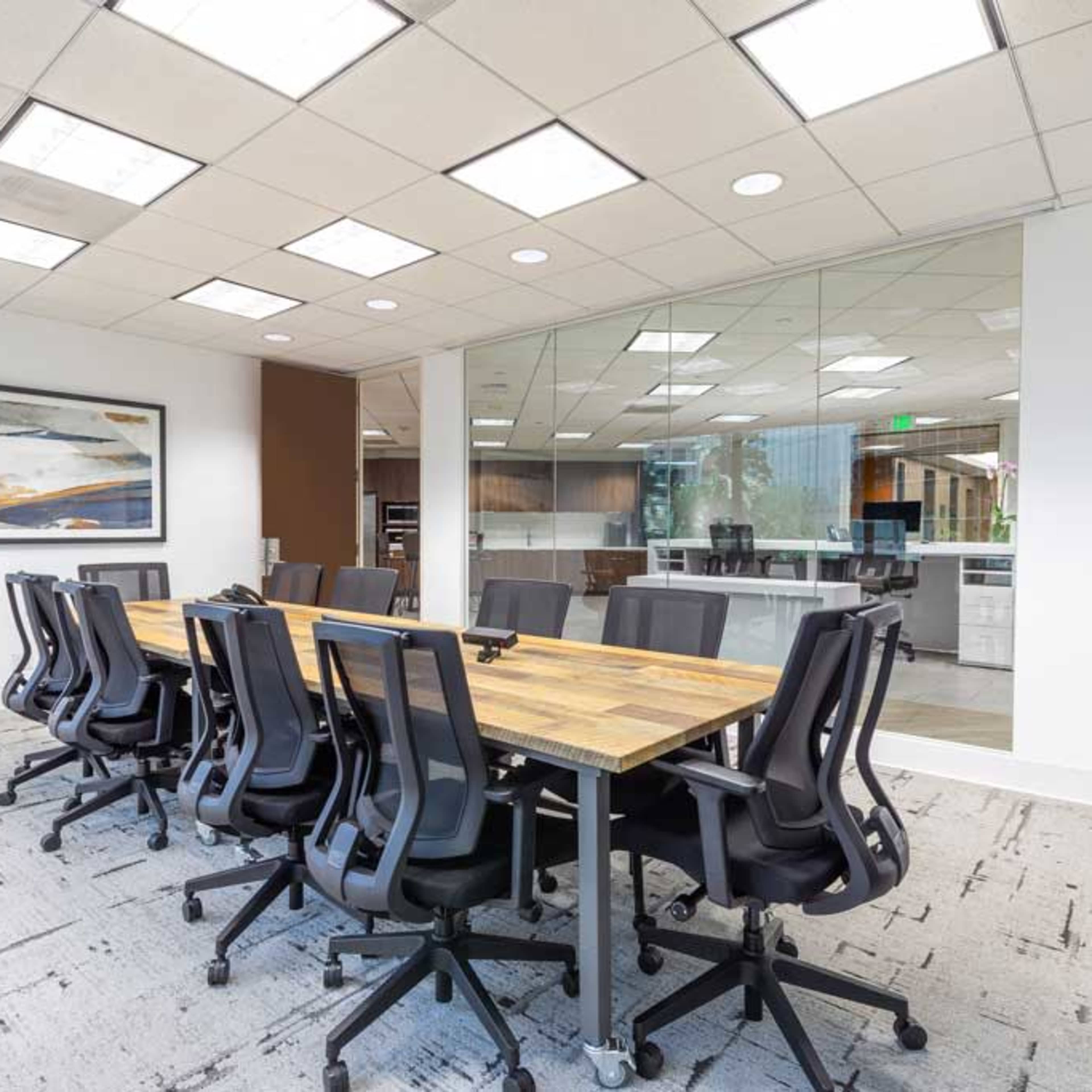 A large conference table with several ergonomic chairs is set up in a modern office space with glass walls.