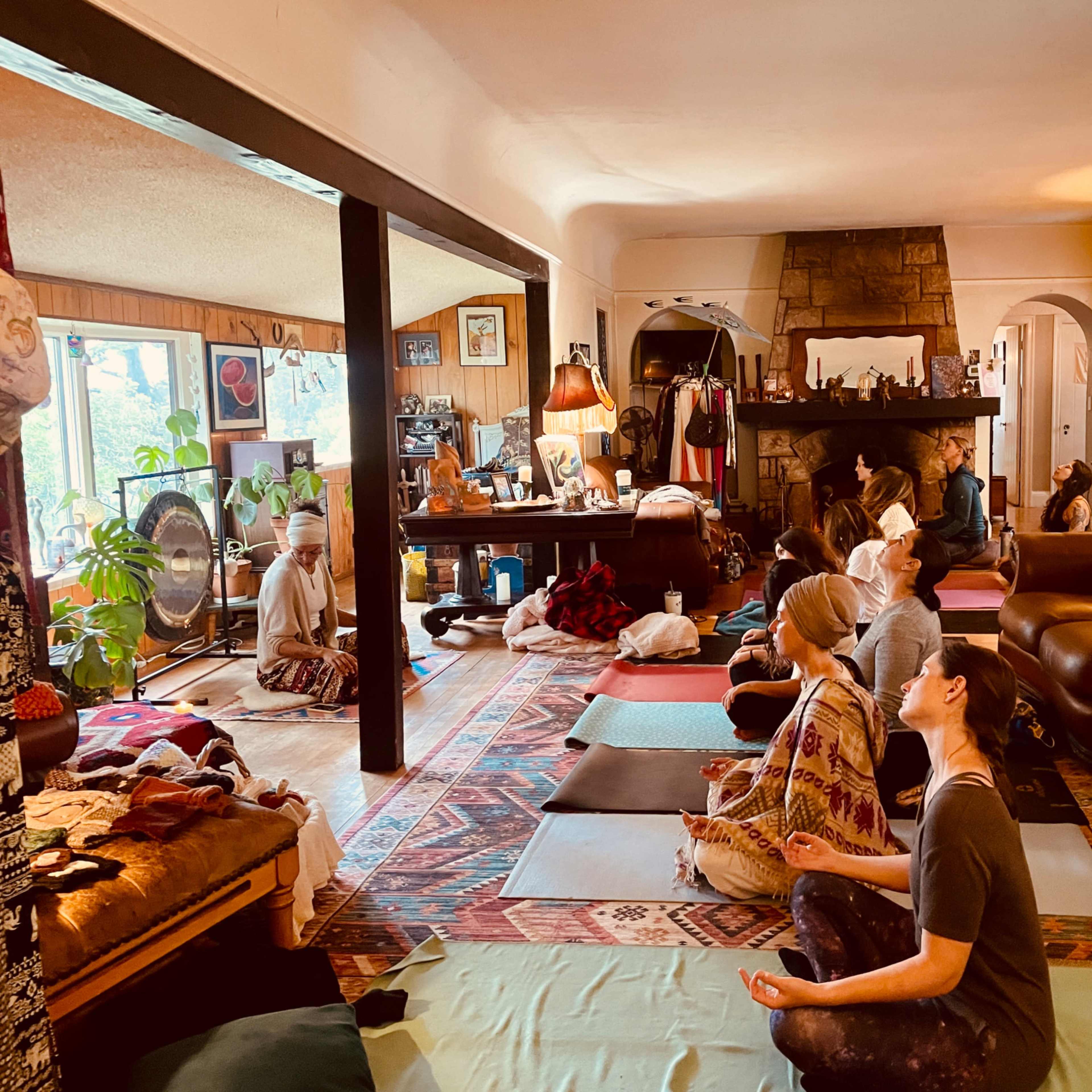 A group of people is practicing meditation in a cozy room filled with comfortable furnishings and natural light.