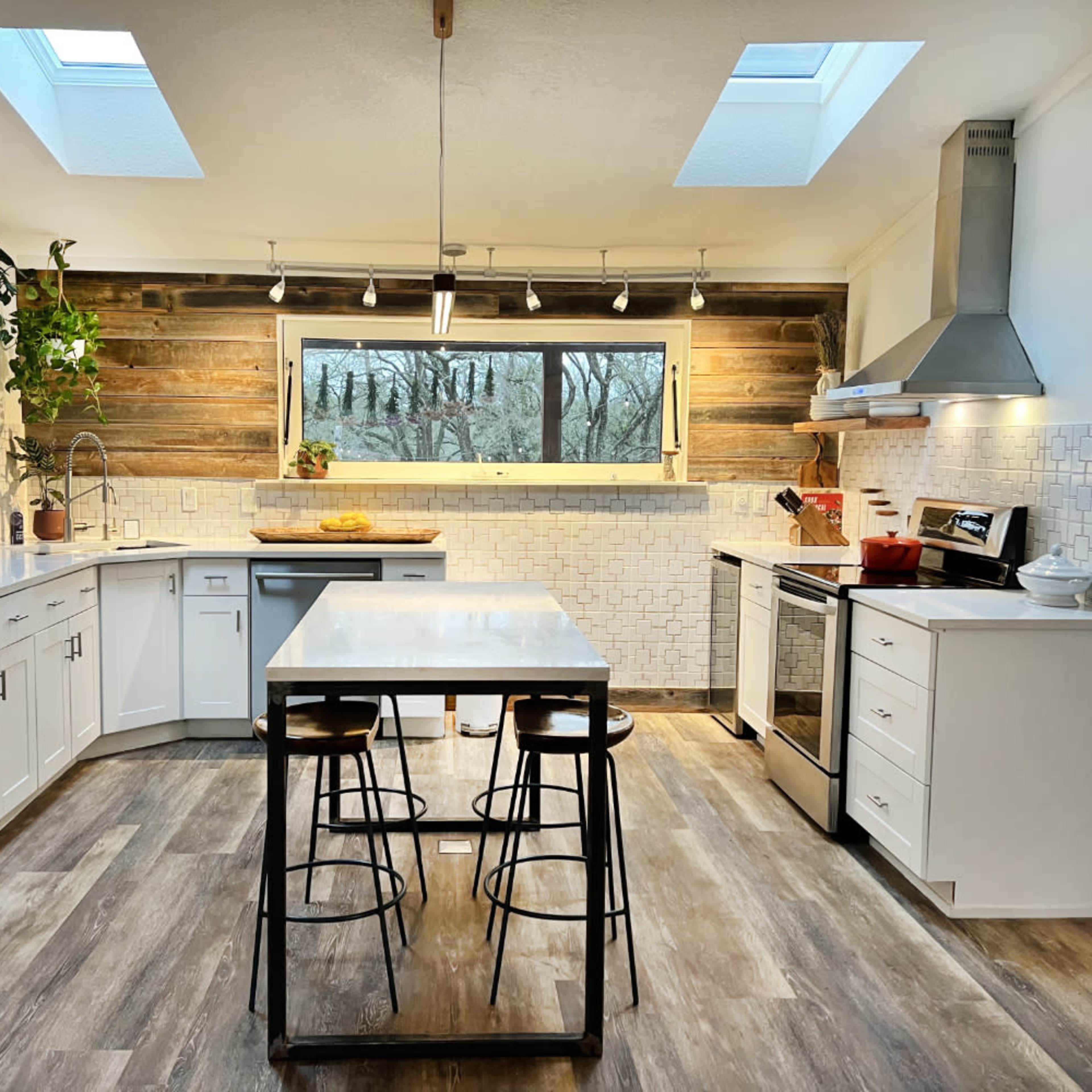 A modern kitchen features a central island with bar stools, white cabinetry, a stainless steel refrigerator, and skylights illuminating the space.